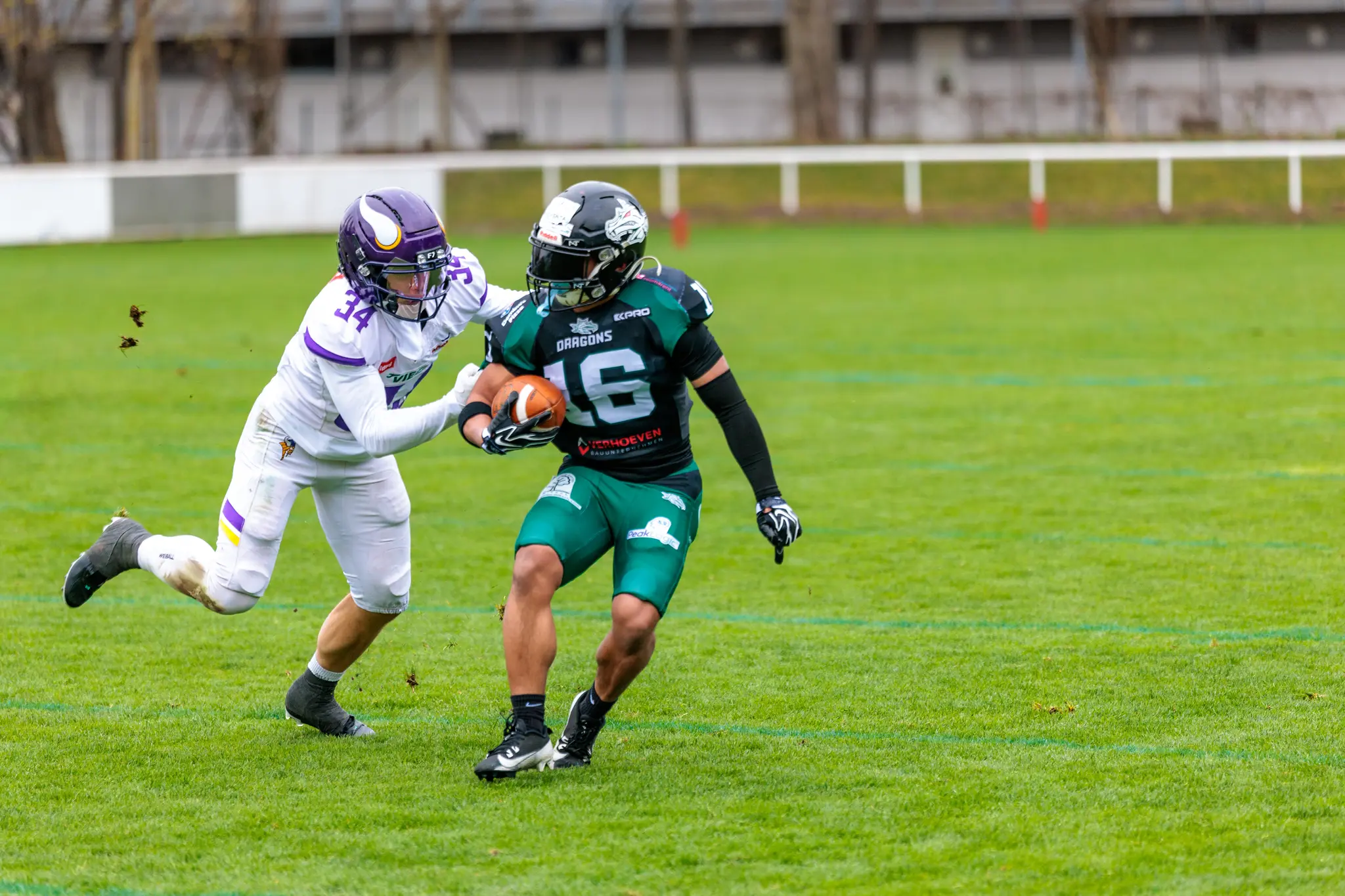 Ein American Football Spieler der Danube Dragons in Grün mit der Nummer 16 läuft mit dem Ball, während ein Vienna Vikings Spieler in Weiß und Lila zum Tackle ansetzt