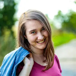 Lächelnde junge Frau mit Jeansjacke im Freien vor unscharfem grünen Hintergrund lens: 56mm F1.4 DC DN | Contemporary 018