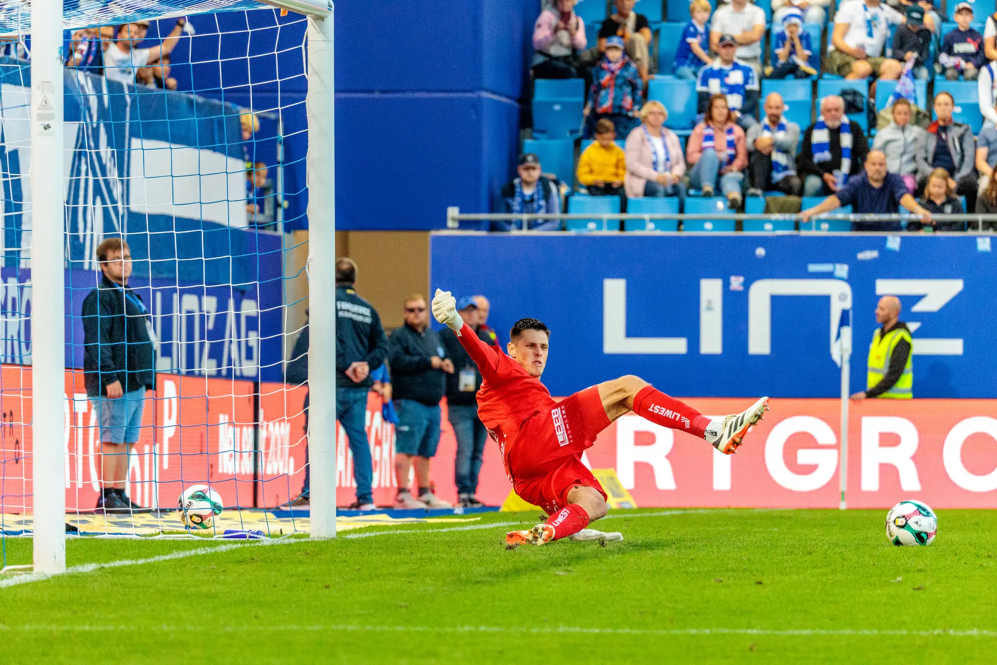Der Torhüter von Blau-Weiß Linz, Viktor Baier, in seinem leuchtend roten Trikot bei einer spektakulären Parade während des Bundesligaspiels gegen Altach