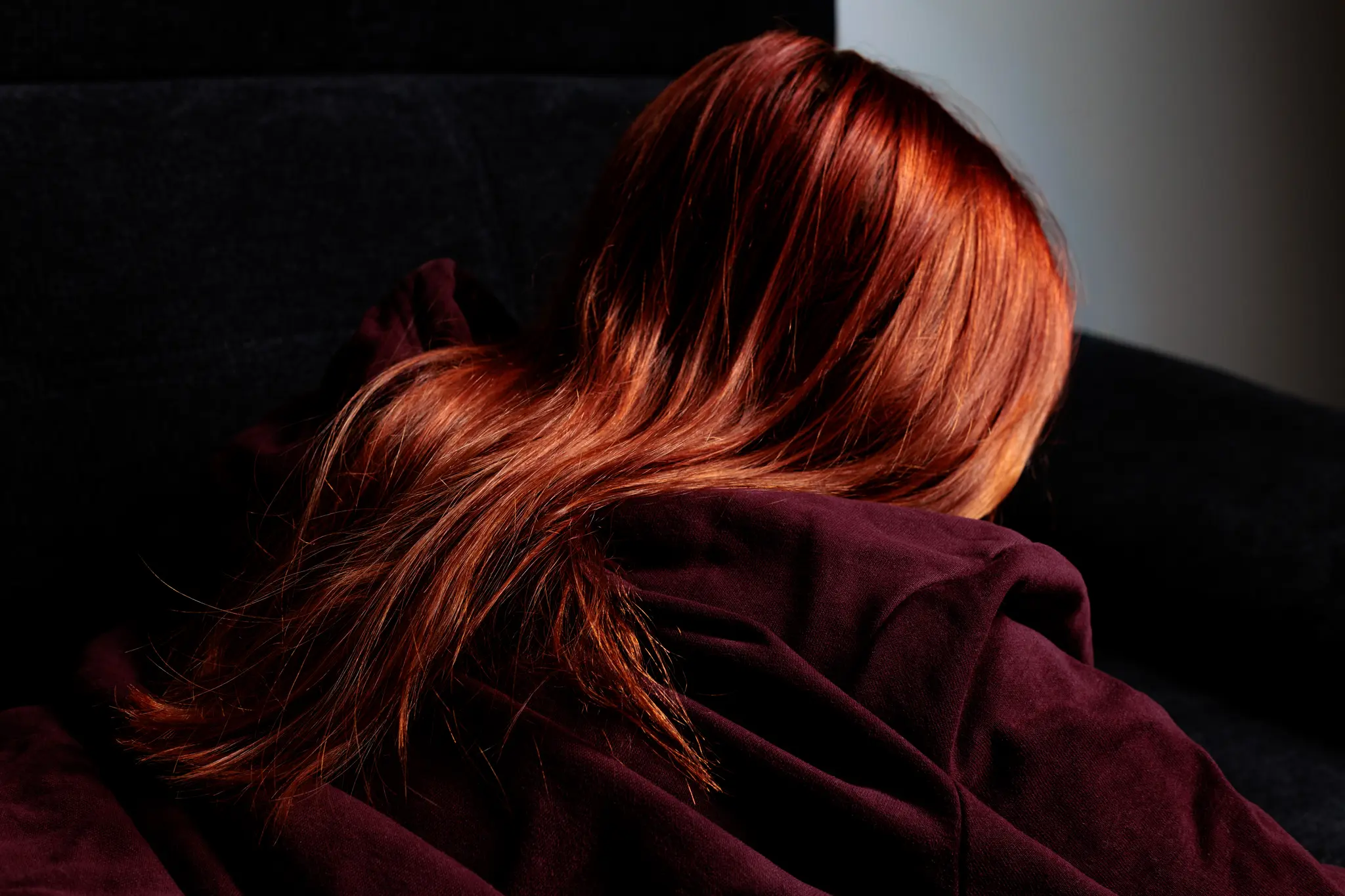 Stimmungsvolles Detailportrait von hinten, das die fließenden roten Haare einer Frau auf einem bordeauxfarbenen Stoff betont