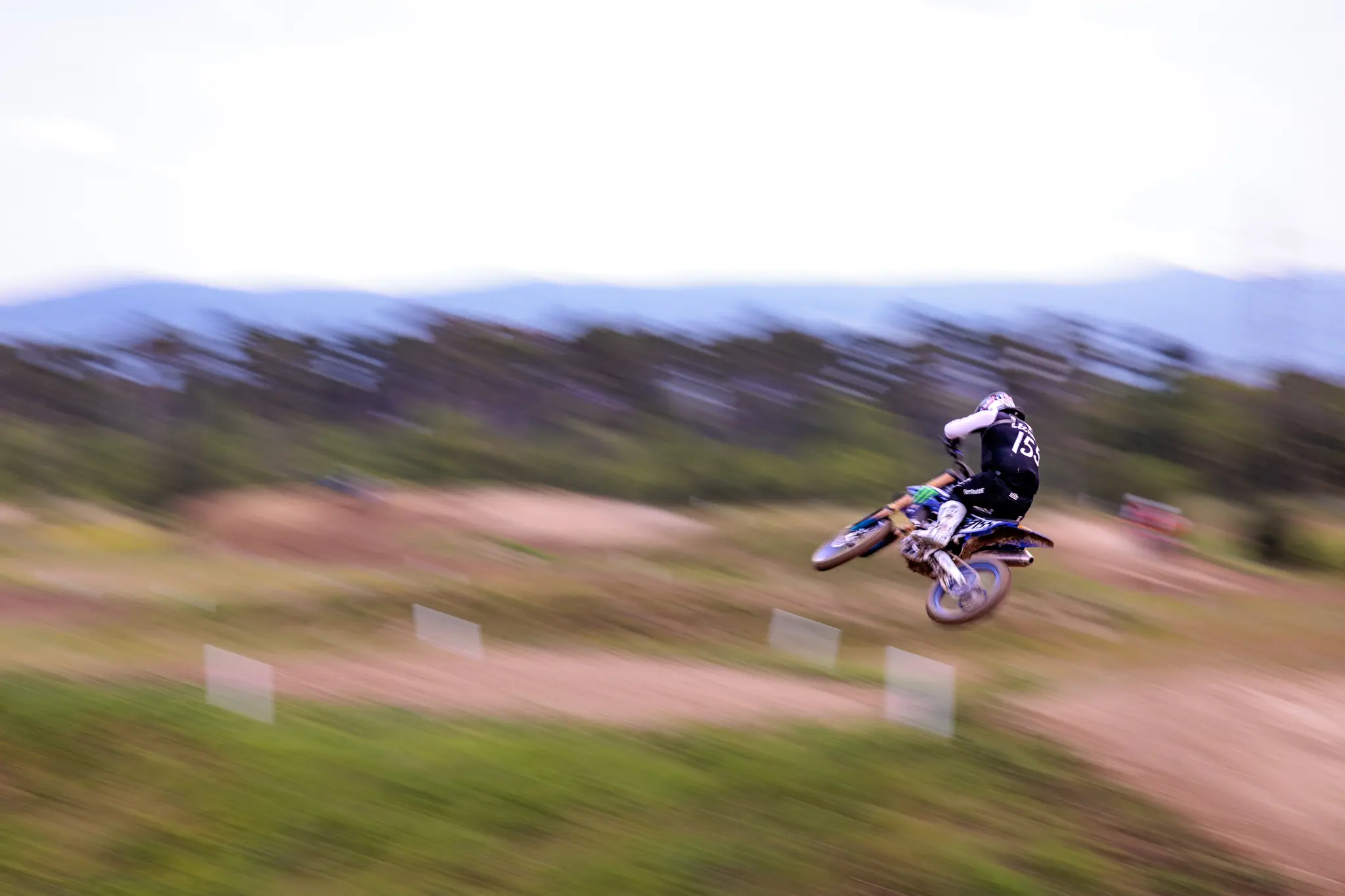 Motocrossfahrer springt auf Motorrad über Rennstrecke, dynamisches Actionfoto mit Bewegungsunschärfe, Motorsport 