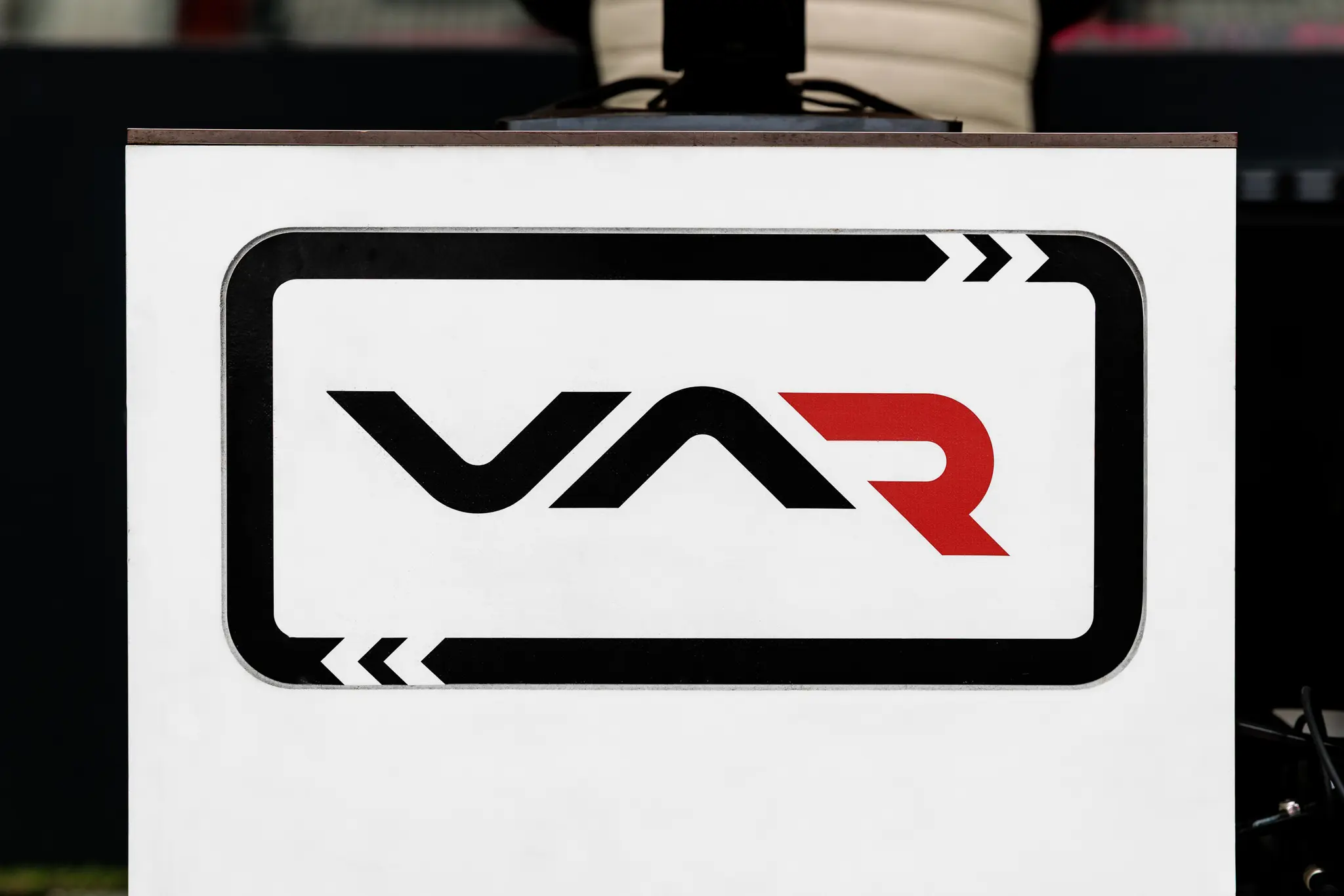 Nahaufnahme eines weißen VAR-Schilds mit dem schwarz-roten Logo, das während eines Fußballspiels zum Videobeweis dient