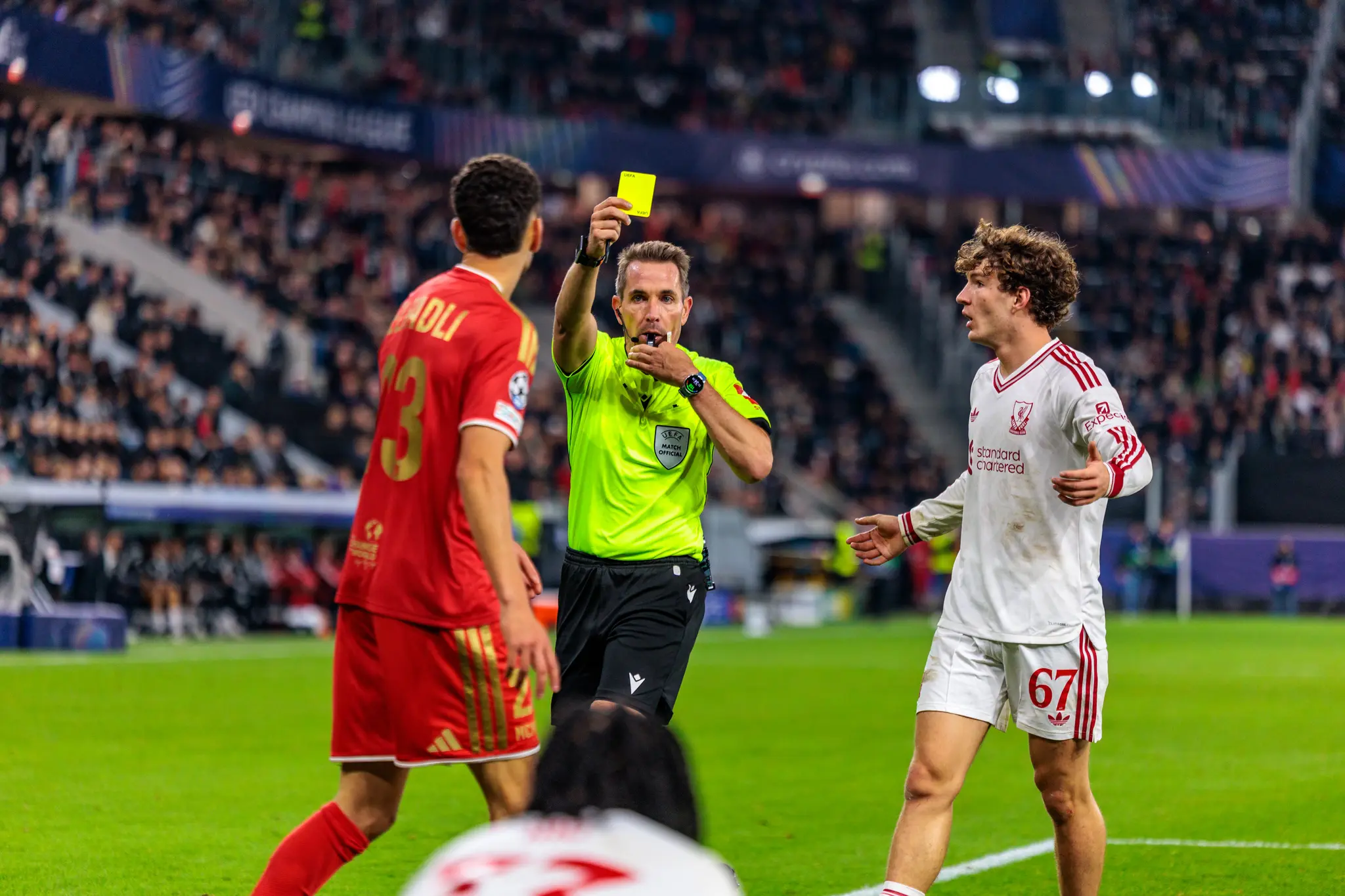 Schiedsrichter Tobias Stieler hebt mit der Pfeife im Mund die Gelbe Karte gegen Daniel Elfadli (23) hoch, Liverpools Koumas (67) beschwert sich über das Foul.