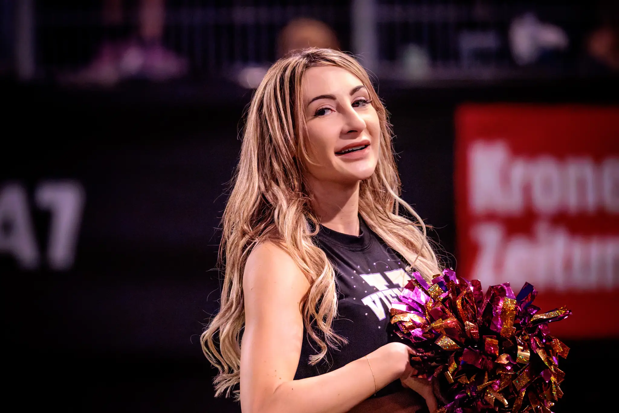 Ein warmer Blick bei Flutlicht: Eine Tänzerin des Vienna Vikings Spirit Squad klemmt ihr violett-goldenes Pompom lässig unterm Arm und lächelt sanft.