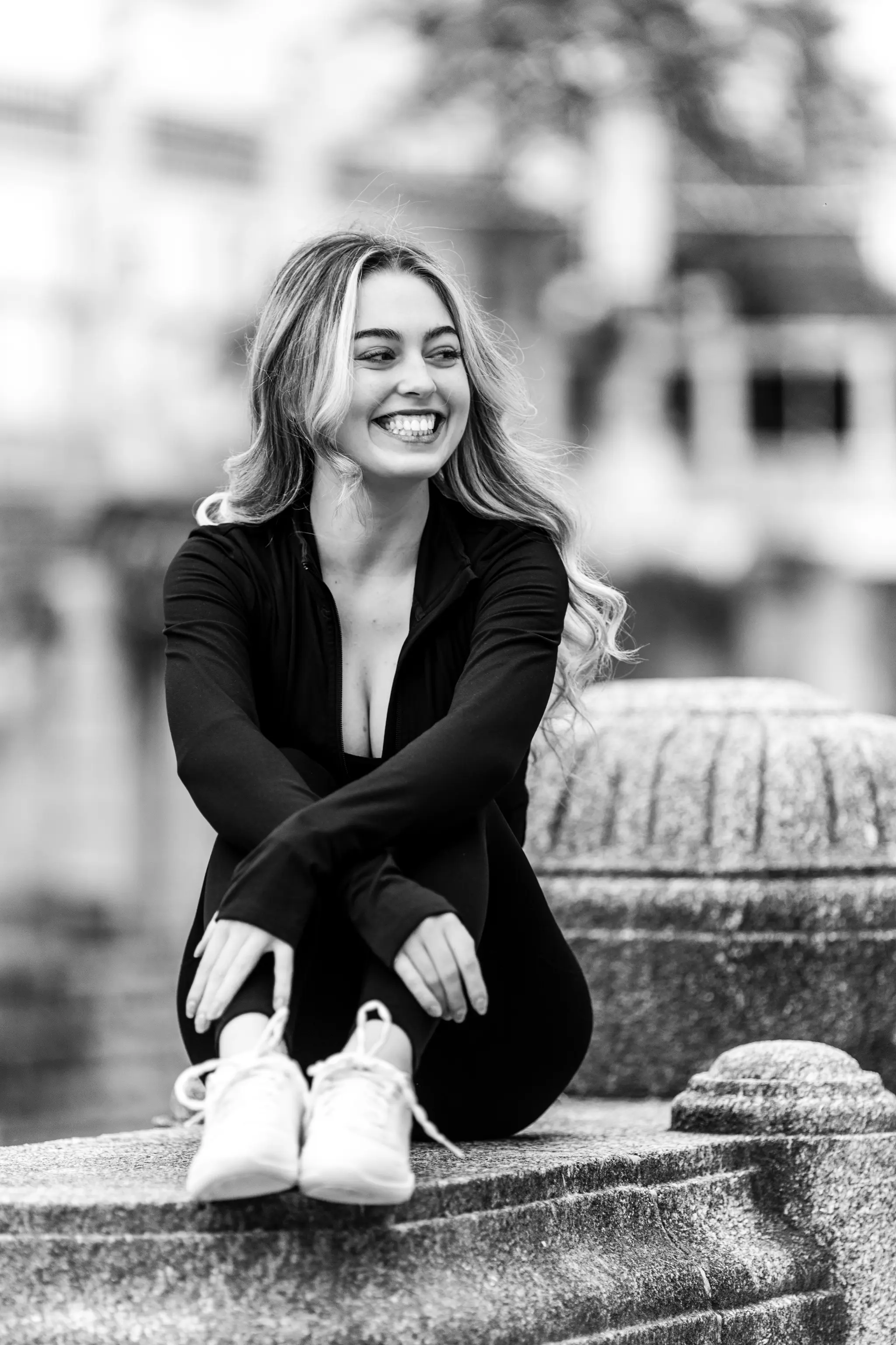 Schwarz-Weiß-Porträt von Model Valentina, die in sportlicher Kleidung lachend auf einer Steinbrüstung im Wiener Stadtpark sitzt