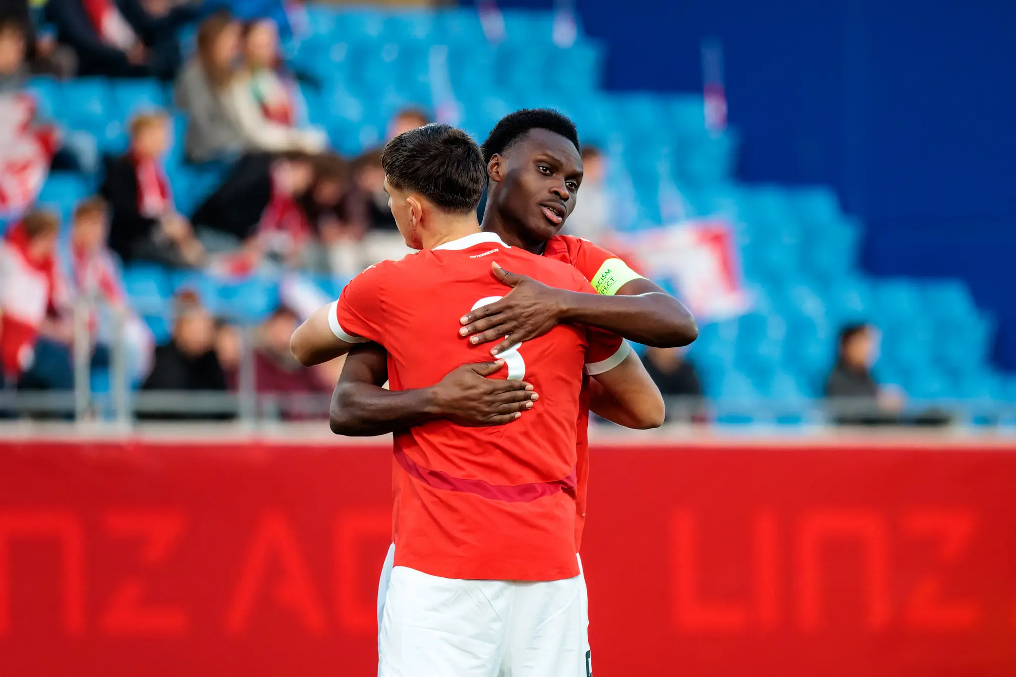 Zwei österreichische U21-Fußballspieler, Samson Baidoo und Tim Trummer, umarmen sich, wobei Baidoo die Kapitänsschleife am linken Arm trägt