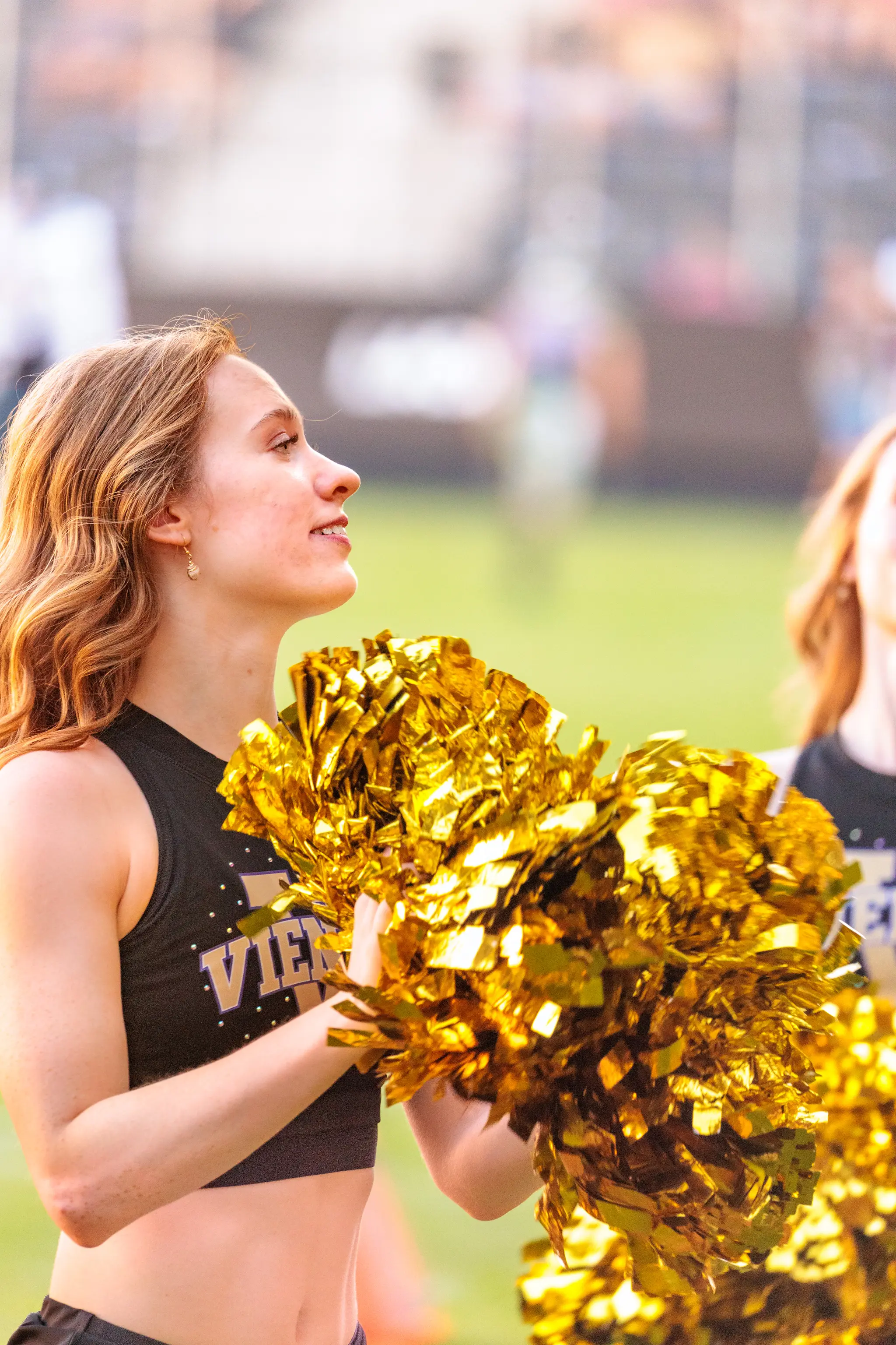 Cheerleaderin der Millennium Dancers mit goldenen Pompons blickt zum Publikum.