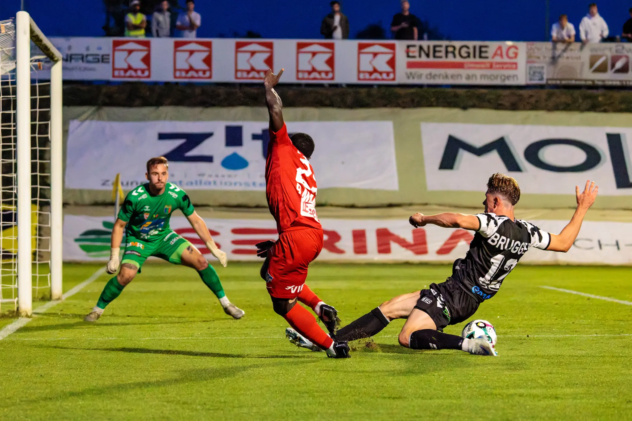 Michael Brugger von SPG HOGO Wels im schwarz-weiß gestreiften Trikot rutscht im ÖFB-Cup im Strafraum in einen Zweikampf um den Ball mit einem Spieler des SKN St. Pölten, während der Welser Torhüter im Hintergrund zuschaut