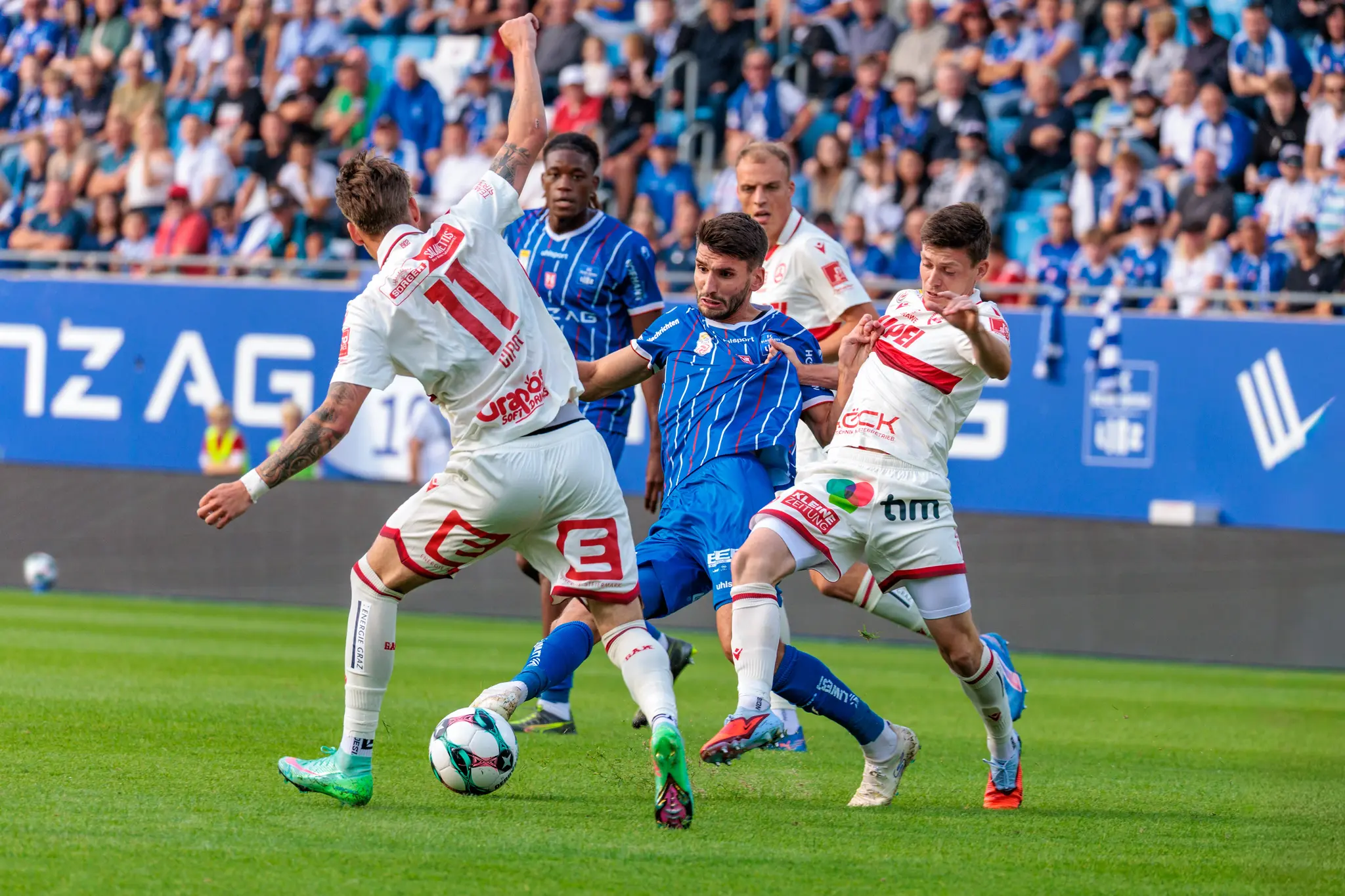 Stürmer Shon Weissman vom FC Blau-Weiß Linz behauptet den Ball in einem intensiven Zweikampf gegen die Verteidiger des GAK während des Bundesligaspiels