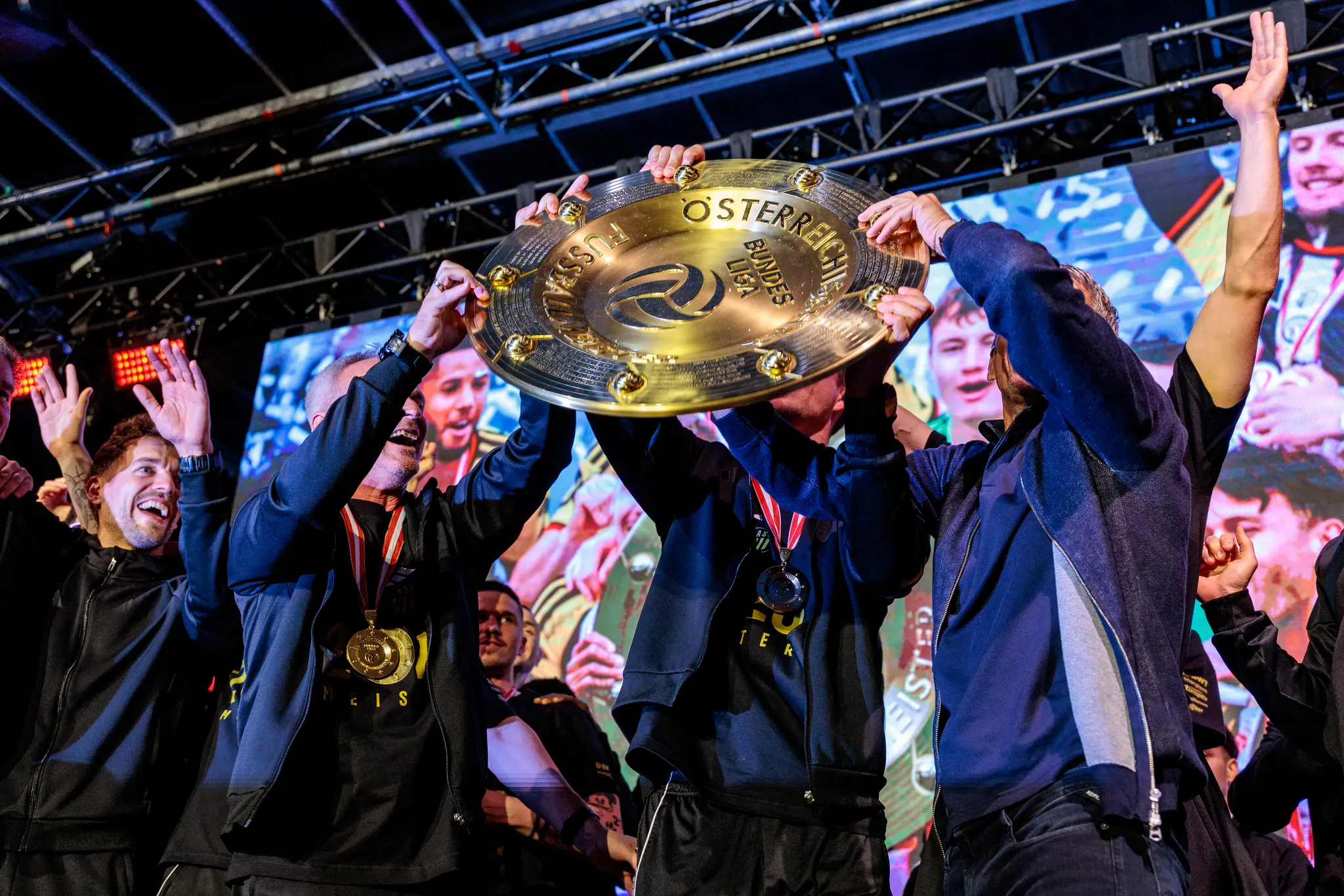 Mehrere Spieler heben gemeinsam den goldenen Meisterteller während der emotionalen Siegerehrung des LASK auf der Bühne
