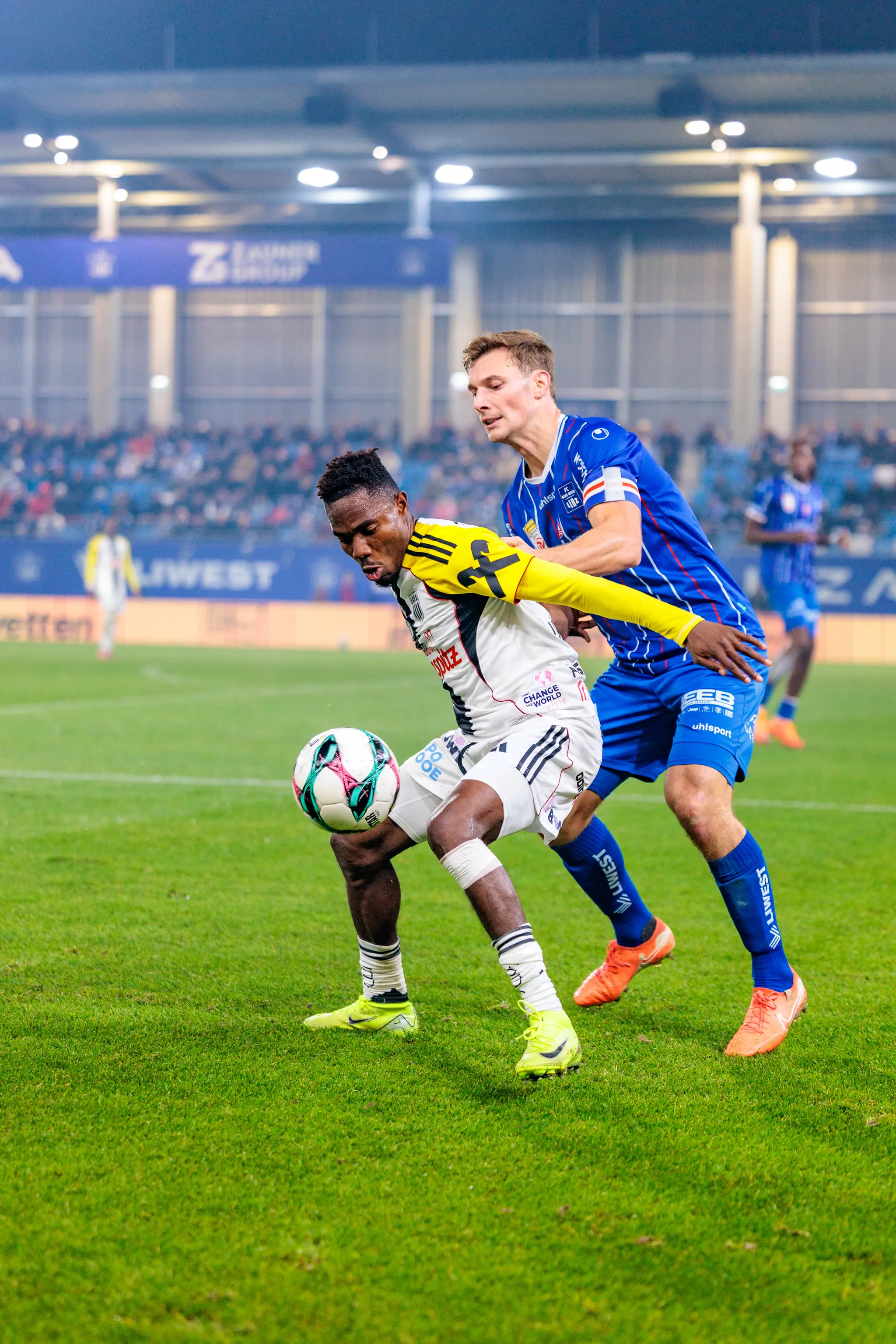 LASK-Spieler George Bello behauptet den Ball in einem intensiven Zweikampf gegen einen Spieler von Blau-Weiß Linz während des Linzer Derbys