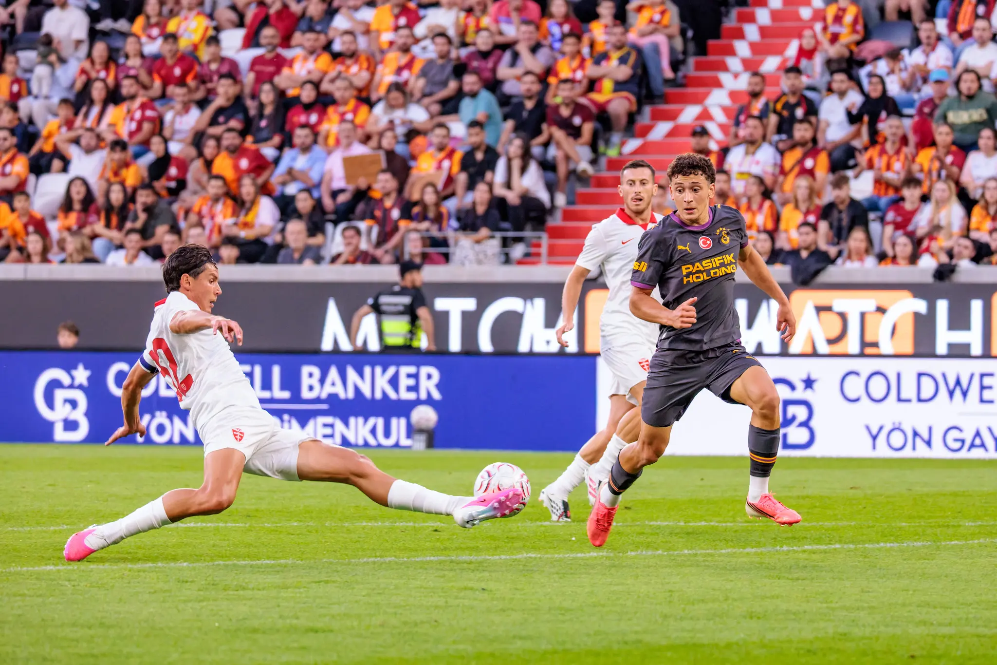 Monza-Spieler grätscht und klärt den Ball, während ein Galatasaray-Spieler im Sprint herannaht.