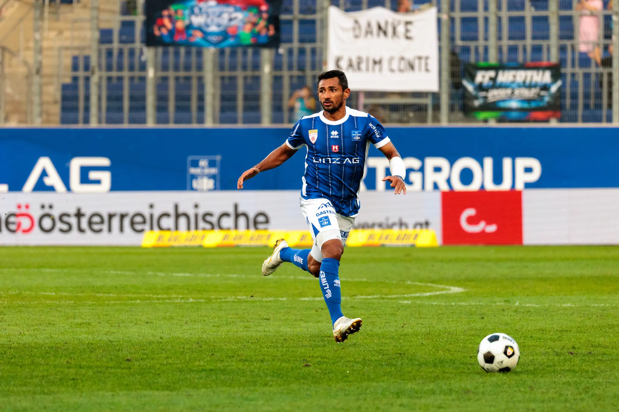 Der Linzer Angreifer Ronivaldo sprintet allein dem freien Ball nach; im Hintergrund ist das Transparent „Danke Karim Conte“ zu lesen, mit dem die Fans den zur Pause ausgewechselten Spieler verabschieden.