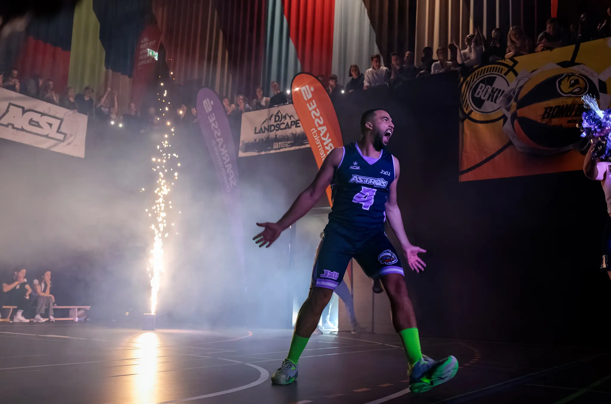 Ein emotionaler Basketballspieler der JKU Astros mit der Nummer 4 stürmt jubelnd unter Funkenregen auf das Spielfeld 