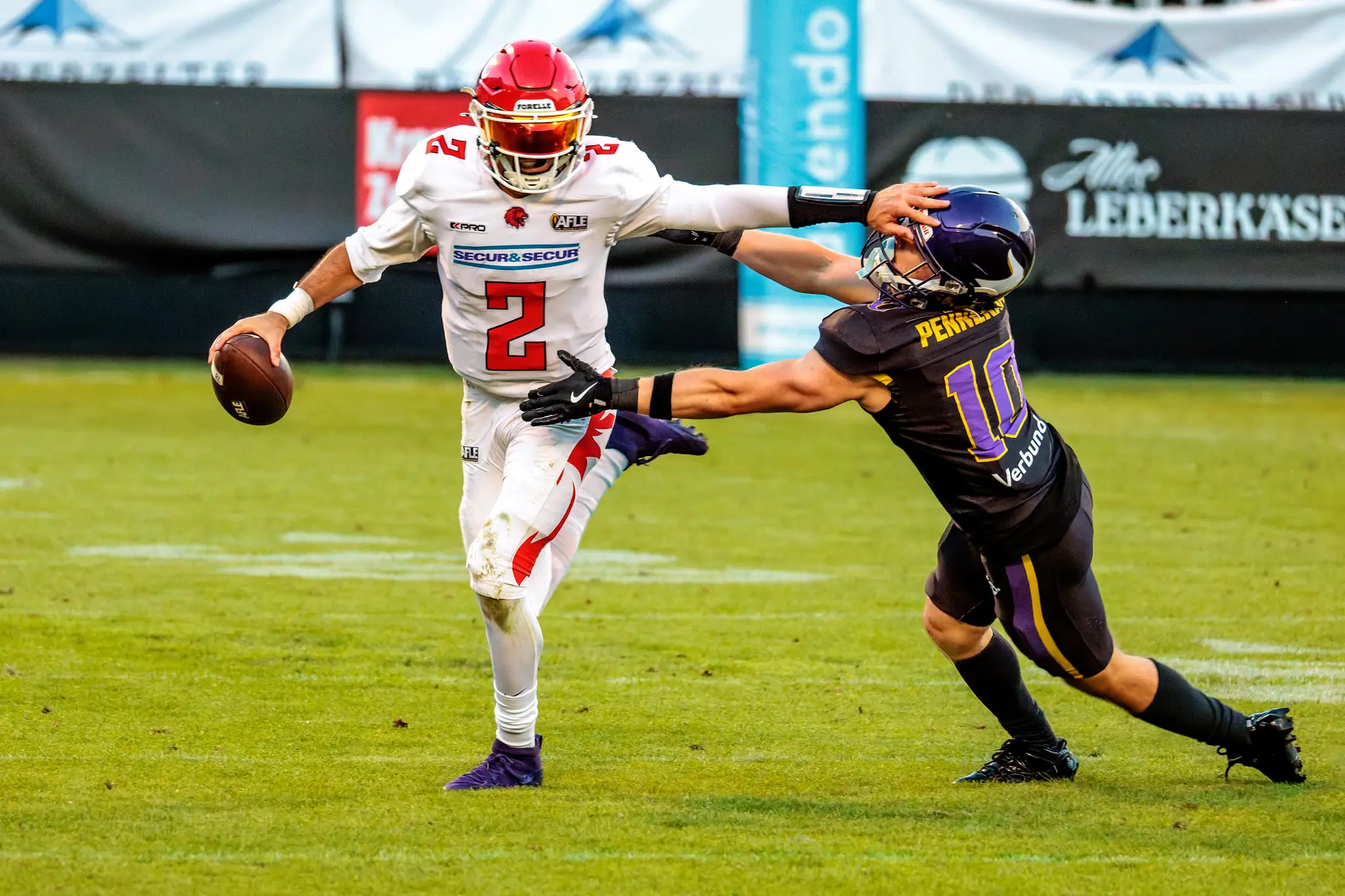 Kämpferisch: Mit ausgestrecktem Arm drängt der Red-Lions-Quarterback (Nr. 2) den Vikings-Verteidiger (10) von sich und verteidigt jeden Zentimeter Raum, den Ball fest in der Rechten.