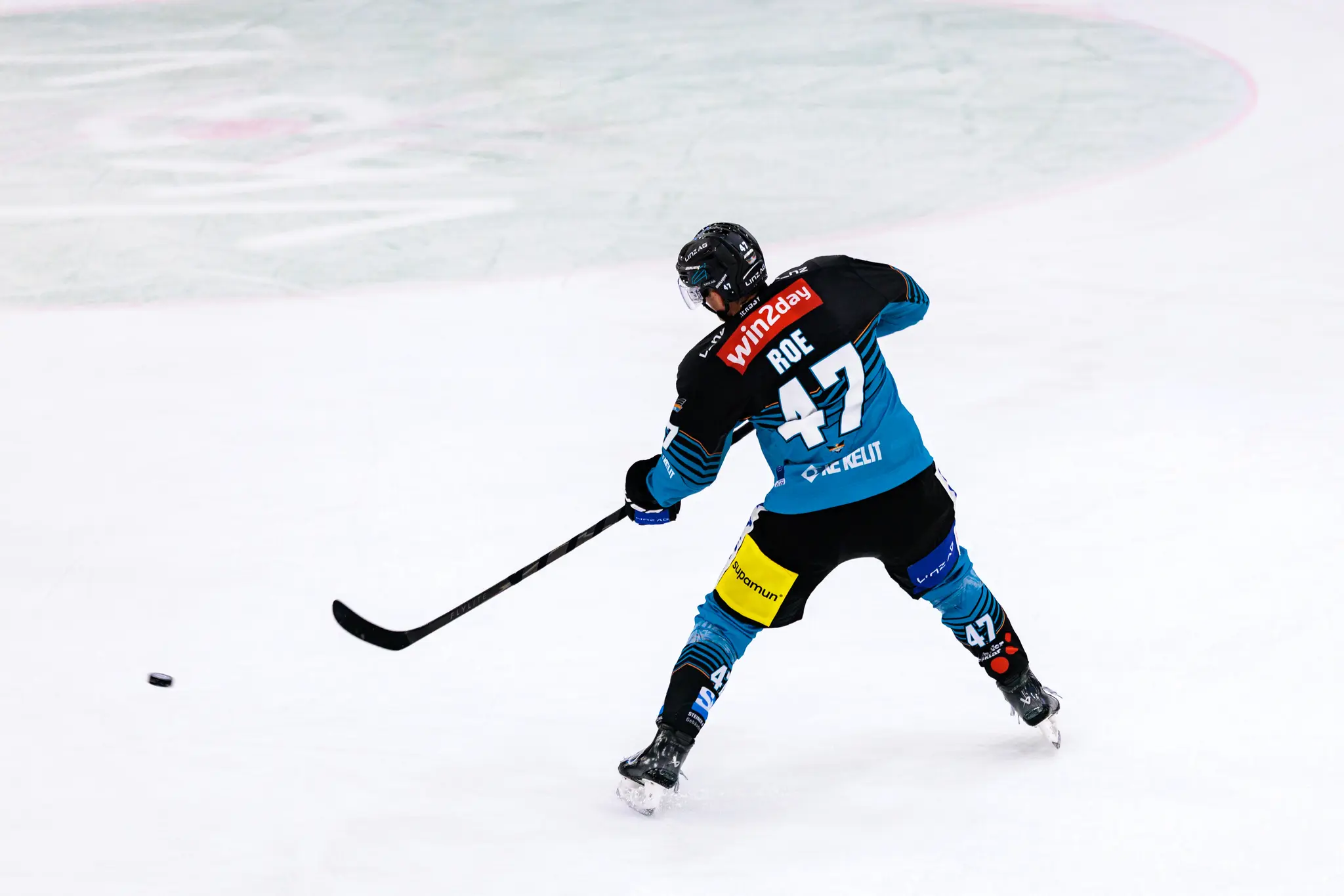 Rückansicht des Eishockeyspielers Logan Roe von den Steinbach Black Wings Linz mit der Nummer 47, der gerade einen kraftvollen Schlagschuss ausführt