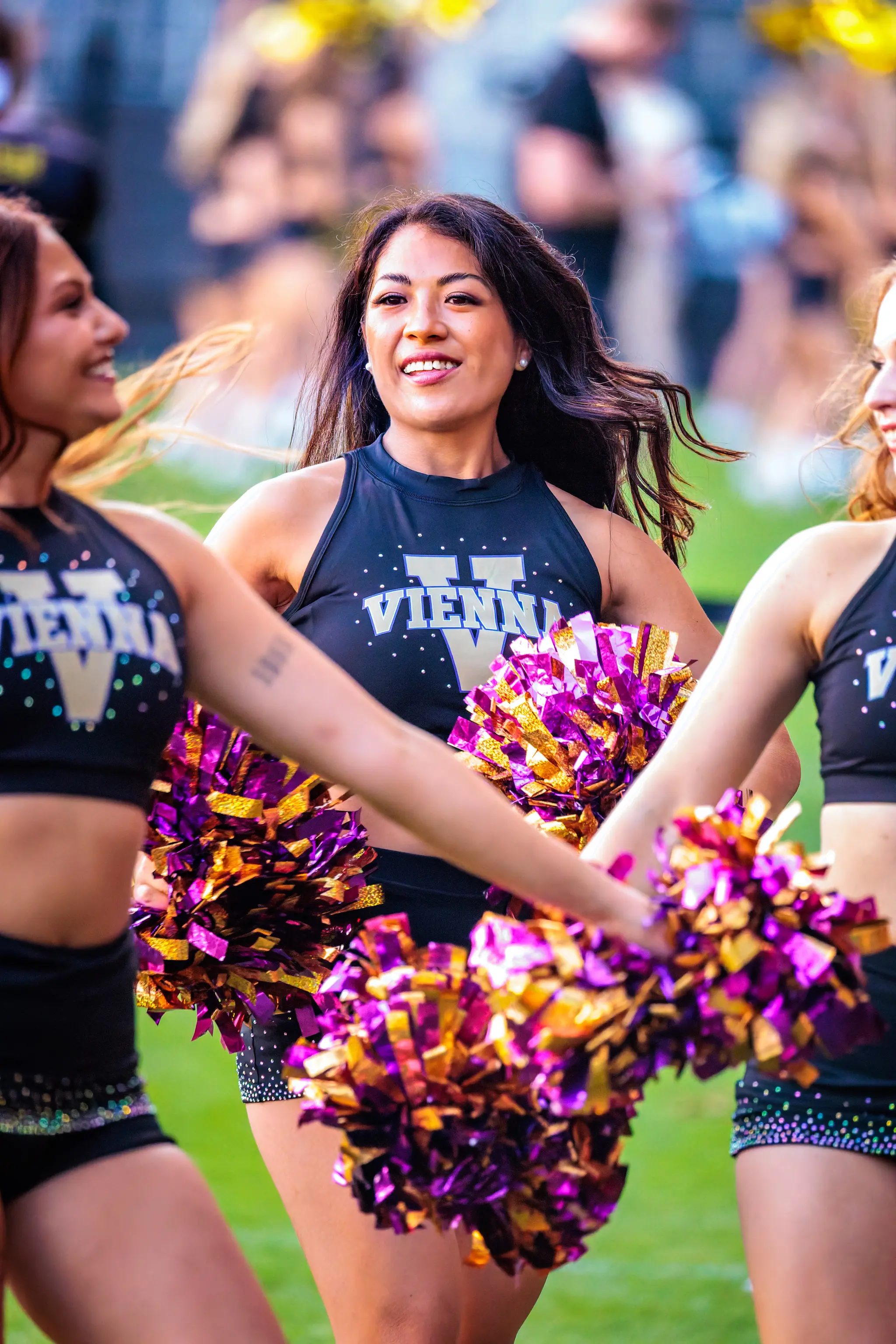 Lächelnd blickt eine Tänzerin des Vienna Vikings Cheer Squads in die Kamera, die lila-goldenen Pompons in den Händen – am Spielfeldrand in einer Spielpause des AFLE-Halbfinales.