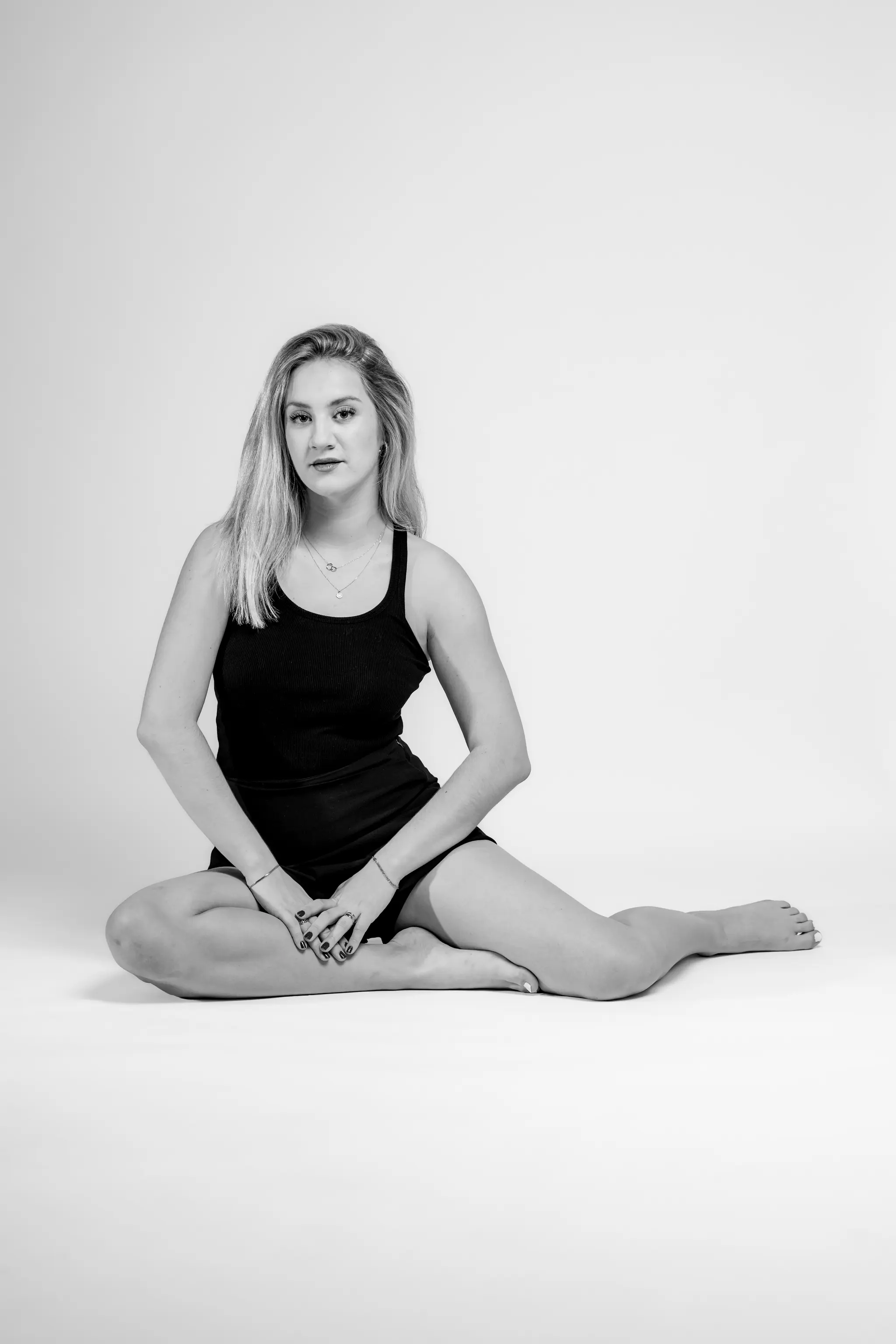 Model Anna sitzt in einem lässigen schwarzen Outfit in einer eleganten Pose auf dem weißen Boden eines Fotostudios und blickt direkt in die Kamera