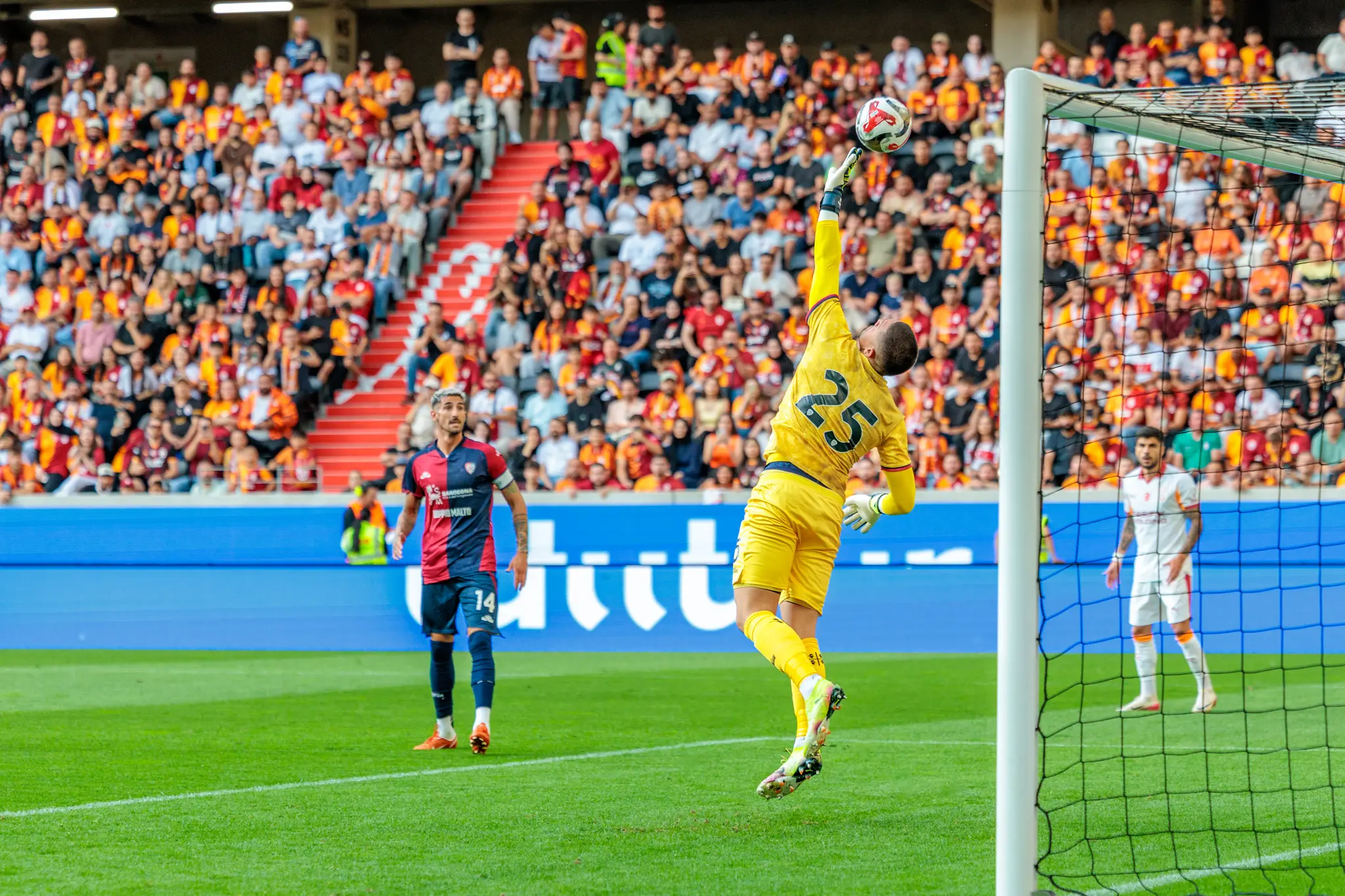 Ein Fußballtorwart in gelbem Trikot springt in der Raiffeisen Arena nach dem Ball, um einen Torschuss während der Nero Summer Series abzuwehren
