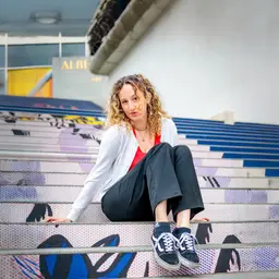 Eine junge Frau mit lockigem Haar sitzt auf einer Treppe mit farbenfrohem Pop-Art-Muster