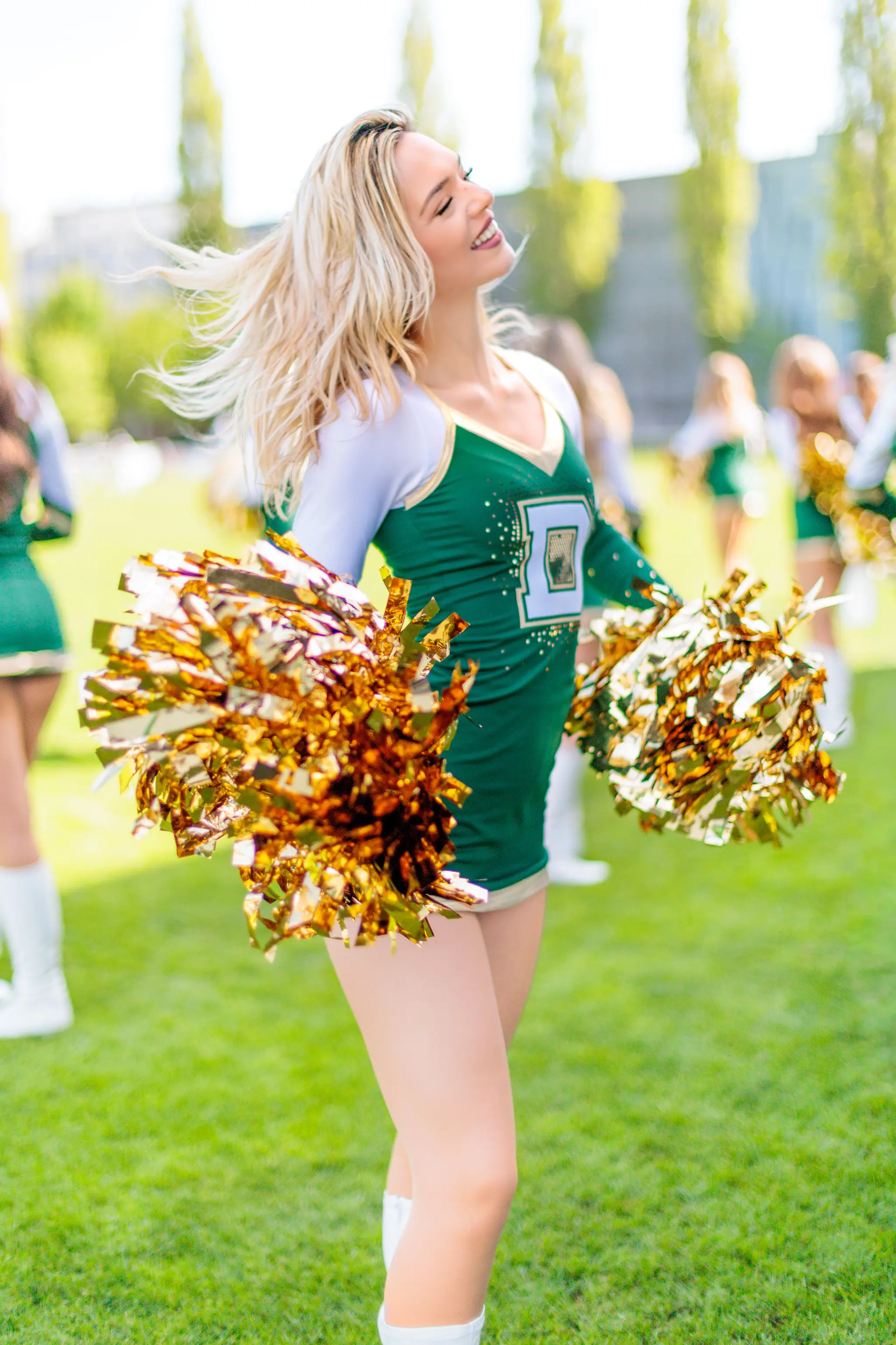 Eine lächelnde Cheerleaderin der Premium Dancers der Danube Dragons mit wehenden blonden Haaren hält ihre glänzenden goldenen Pompoms während eines Auftritts in der Austrian Football League
