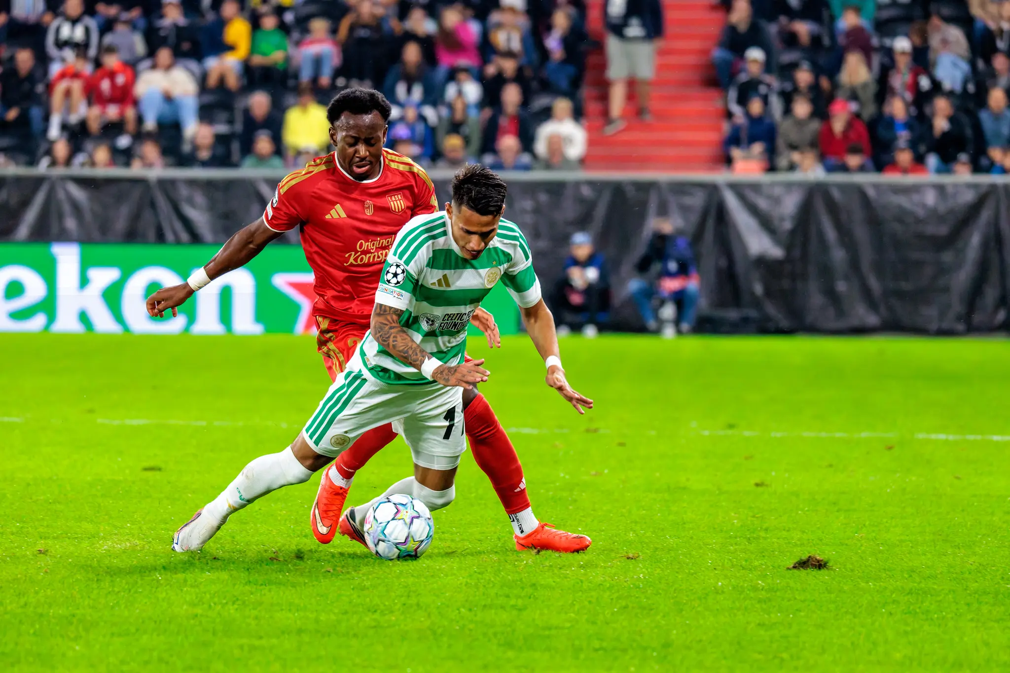 Celtic-Spieler verliert im Zweikampf das Gleichgewicht und fällt nach vorn, während ein LASK-Verteidiger eng dran bleibt und den Ball attackiert.