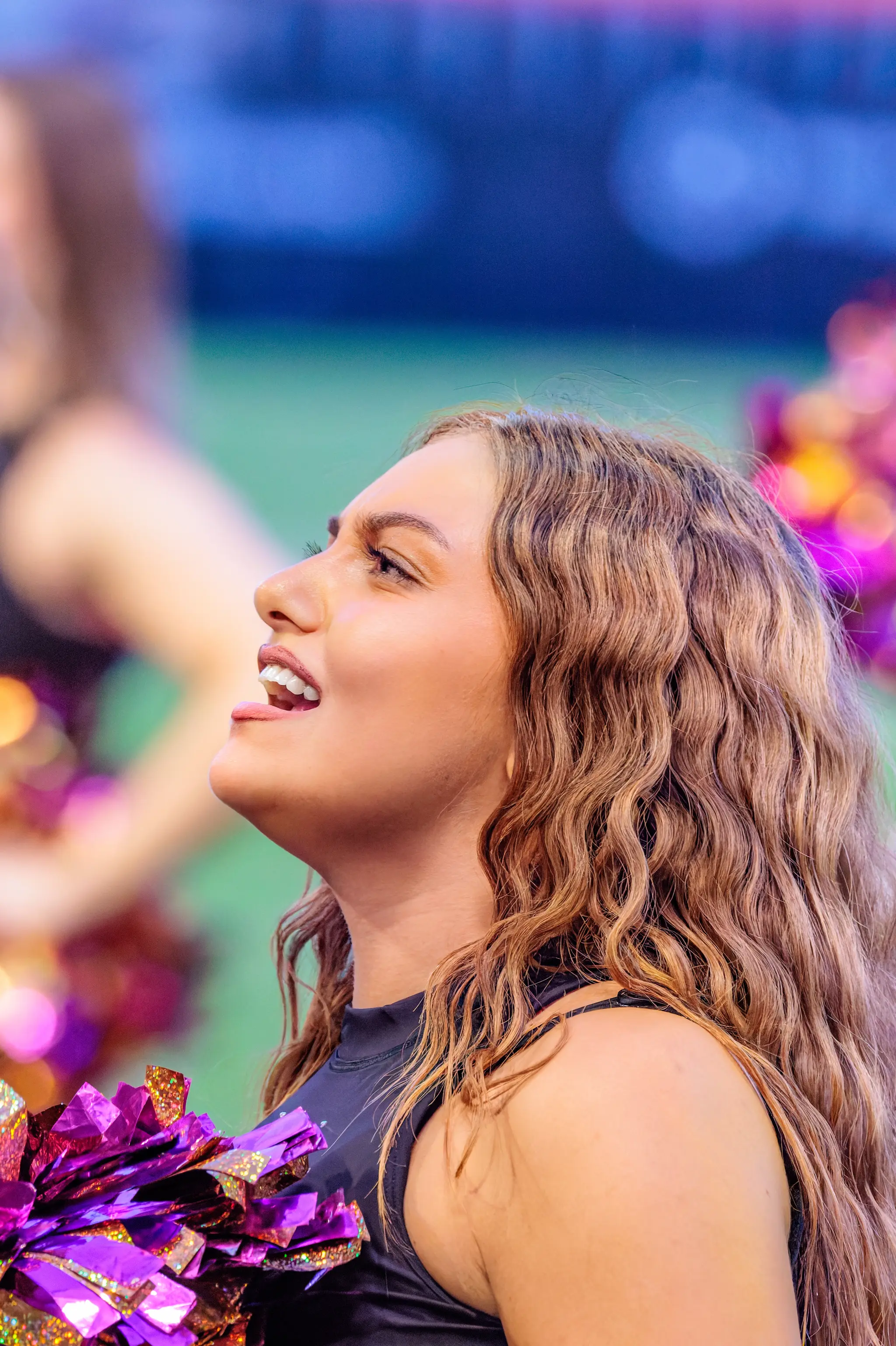 Cheerleaderin des Spirit Squad feuert die Defense an und blickt nach oben, einen violett-goldenen Pompon an der Seite.