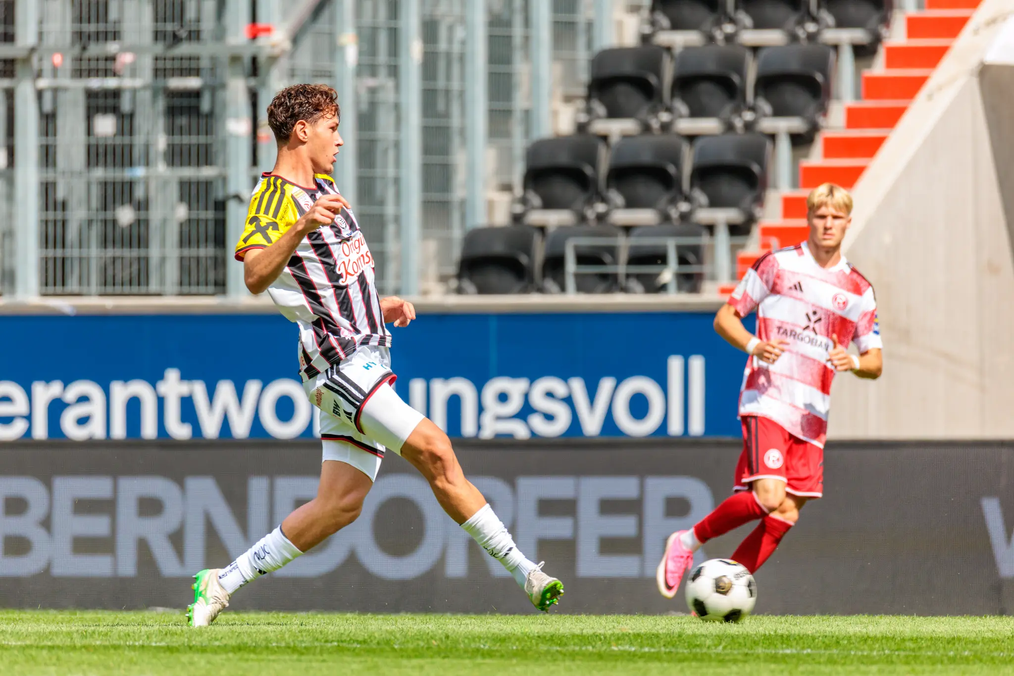 LASK-Spieler sprintet mit Ball am Fuß über das Spielfeld, ein Düsseldorfer Gegenspieler verfolgt ihn im Hintergrund.