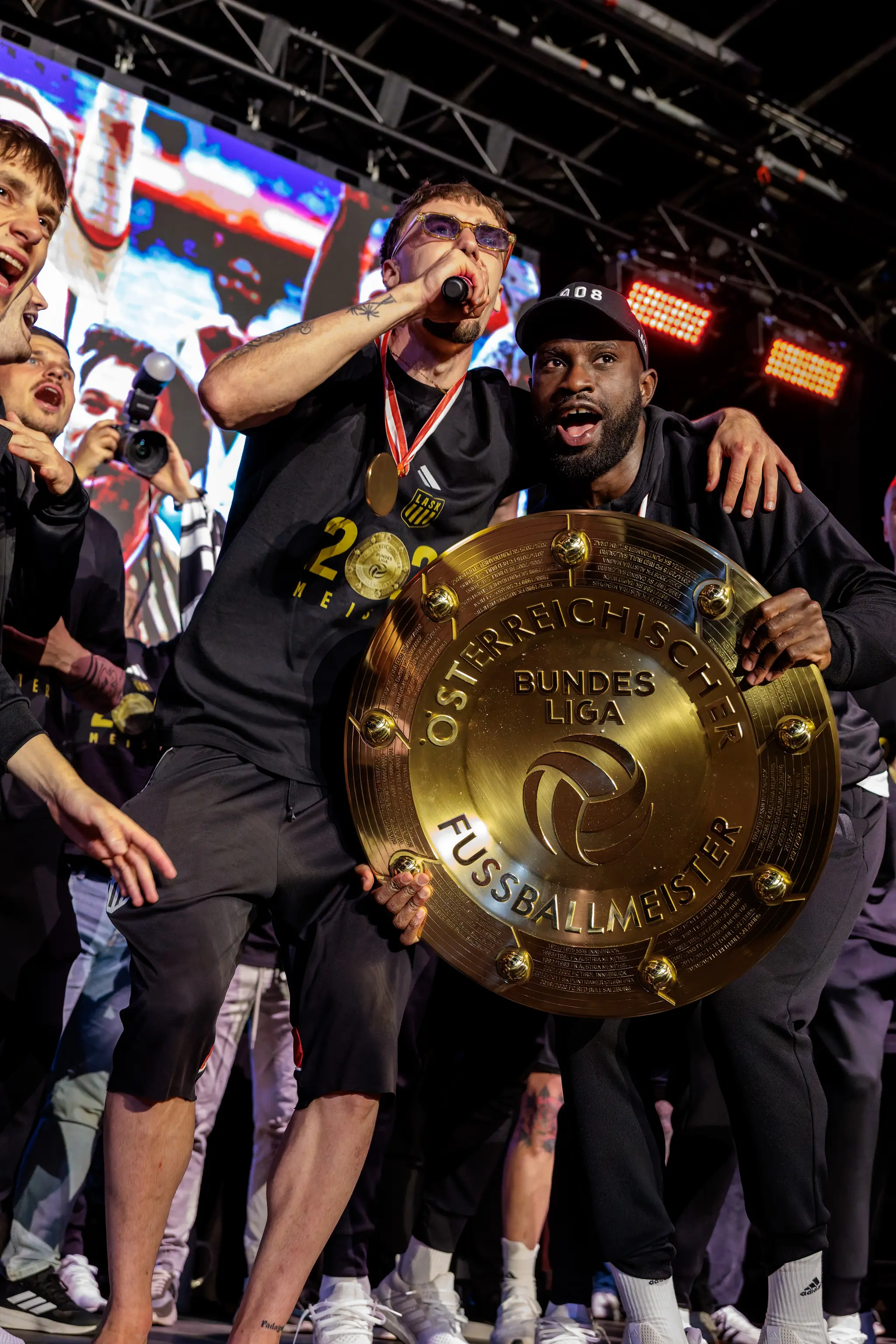 Zwei Spieler des LASK präsentieren gemeinsam den goldenen Meisterteller während der emotionalen Feier in der Fanzone der Raiffeisen Arena