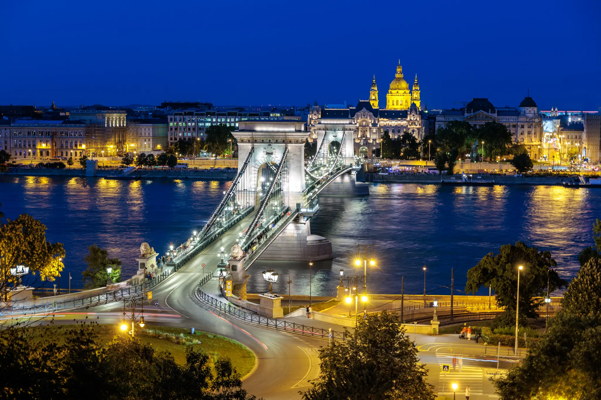 Beleuchtete Kettenbrücke und St.-Stephans-Basilika in Budapest bei Nacht über der Donau mit Lichtspuren. 