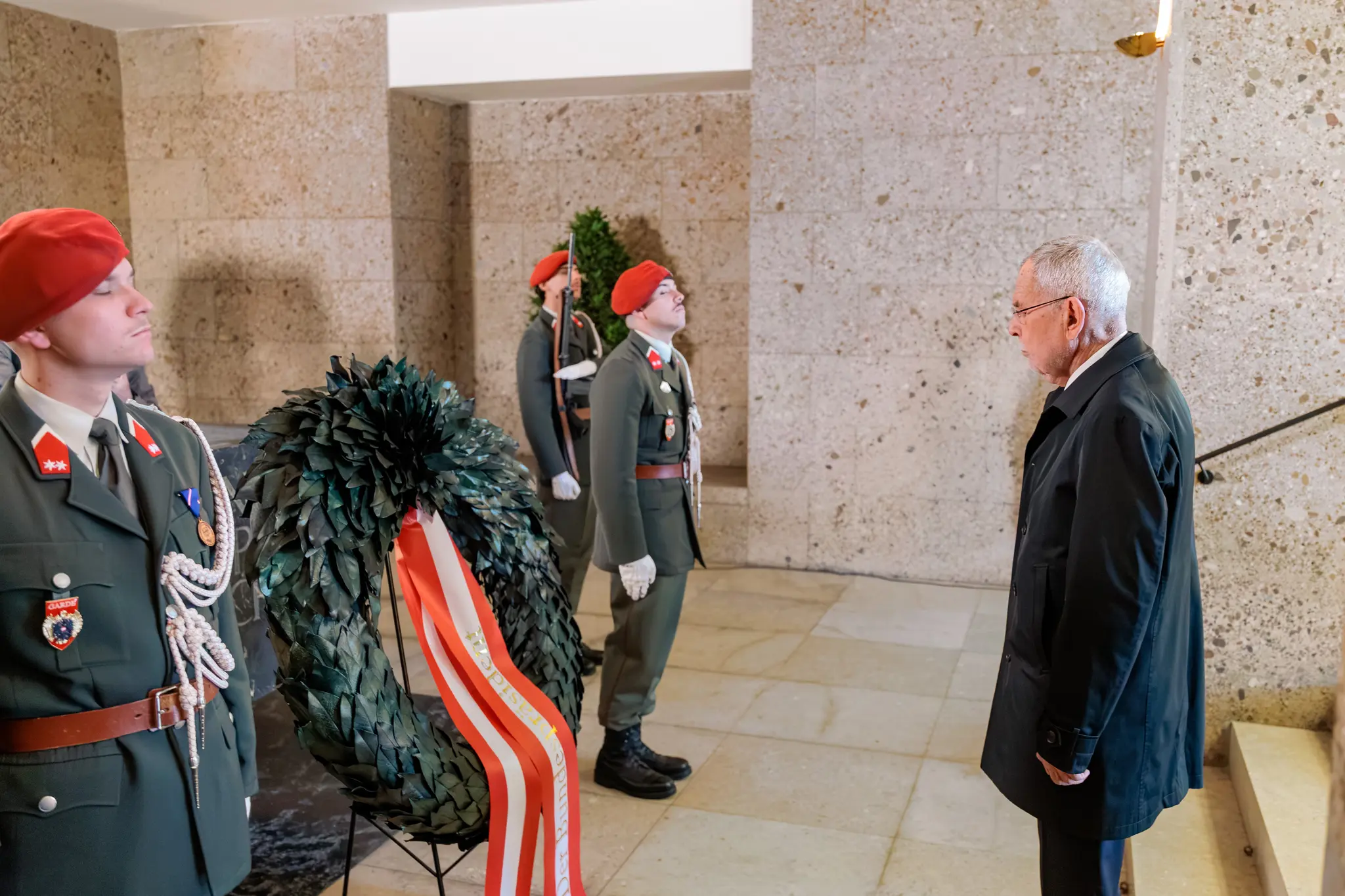 Bundespräsident Alexander Van der Bellen steht mit gesenktem Blick vor einem Kranz im Weiheraum des Äußeren Burgtors, daneben halten Gardesoldaten Wache.