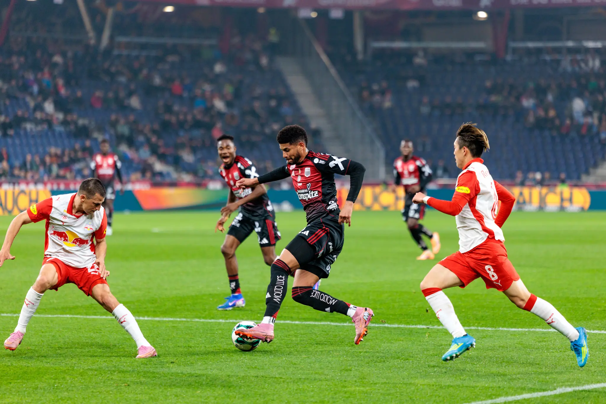 Ein LASK-Spieler setzt sich im Dribbling mit dem Ball am Fuß gegen zwei defensiv agierende Spieler von Red Bull Salzburg durch