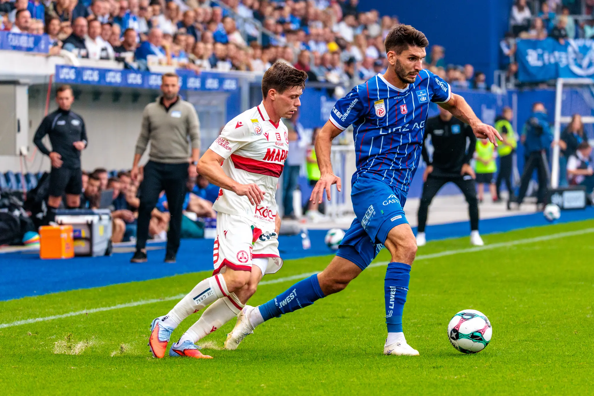 Stürmer Shon Weissman vom FC Blau-Weiß Linz führt den Ball im Dribbling, während ein Gegenspieler des GAK ihn in einem Zweikampf zu stoppen versucht