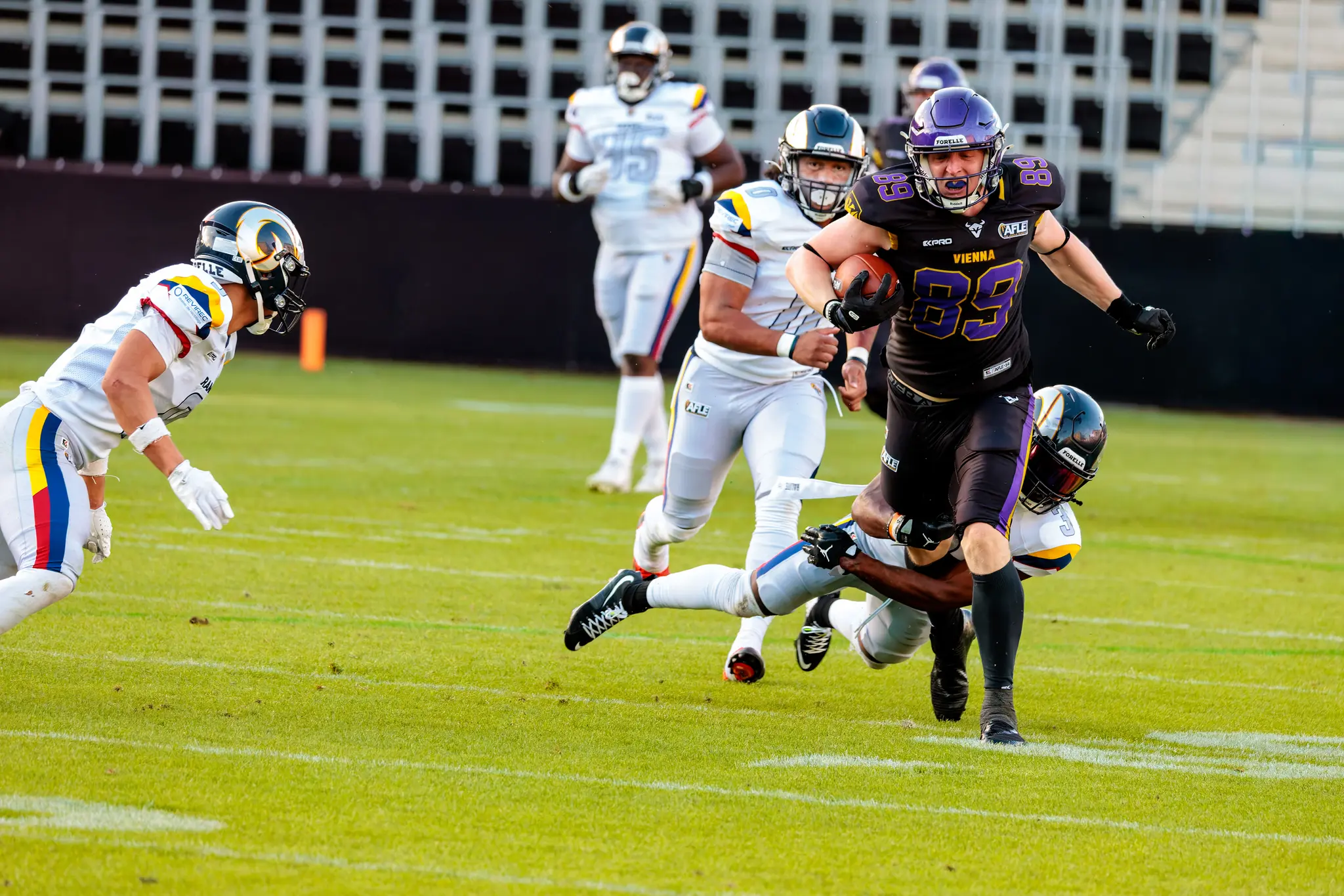Ein Spieler der Vienna Vikings mit der Nummer 85 hält den Ball während eines intensiven Tacklings im AFLE Spiel gegen die Alpine Rams