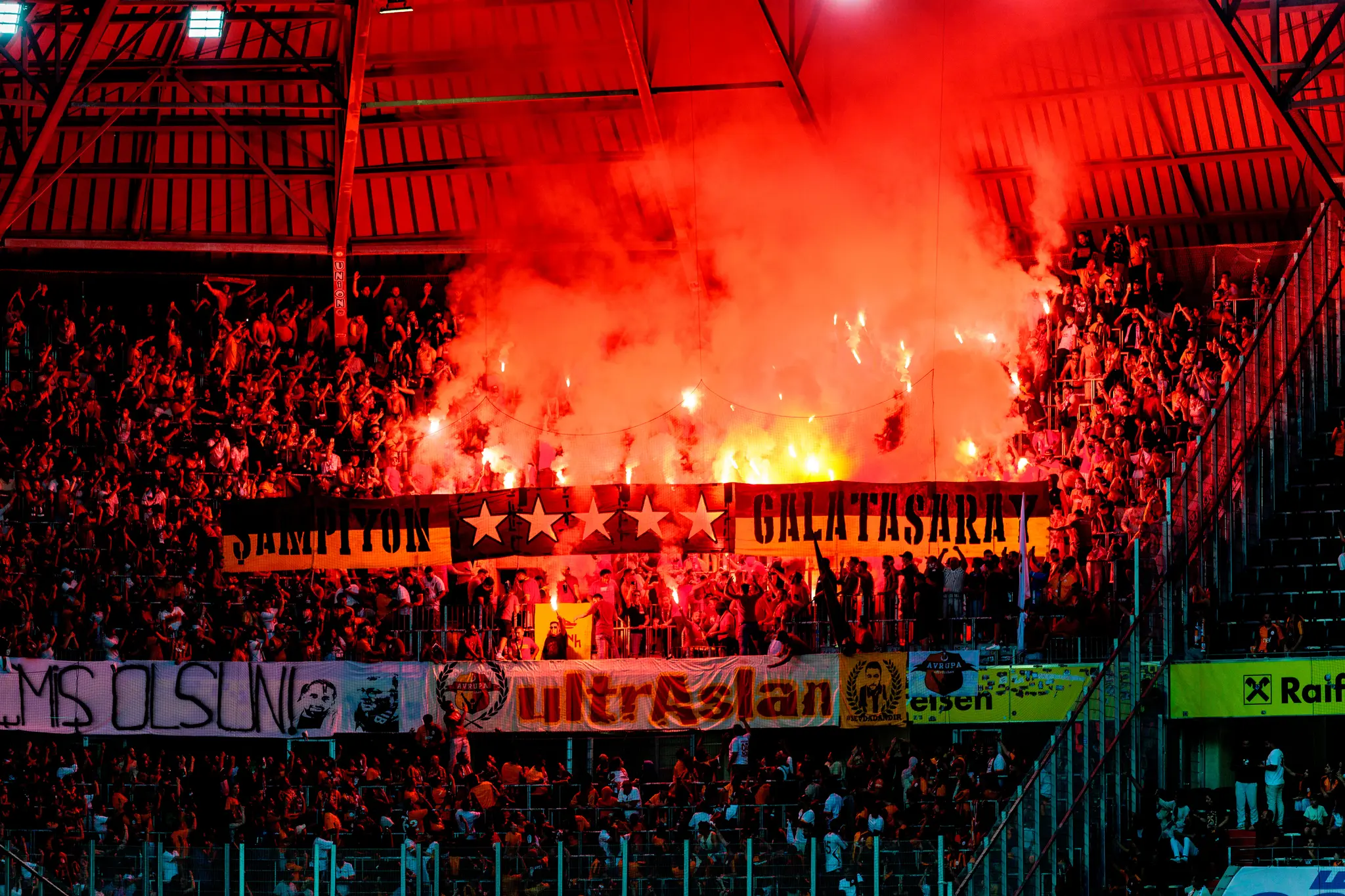 Galatasaray-Fans schaffen in einem Fußballstadion eine leidenschaftliche Atmosphäre mit zahlreichen roten Fackeln und aufsteigendem Rauch 