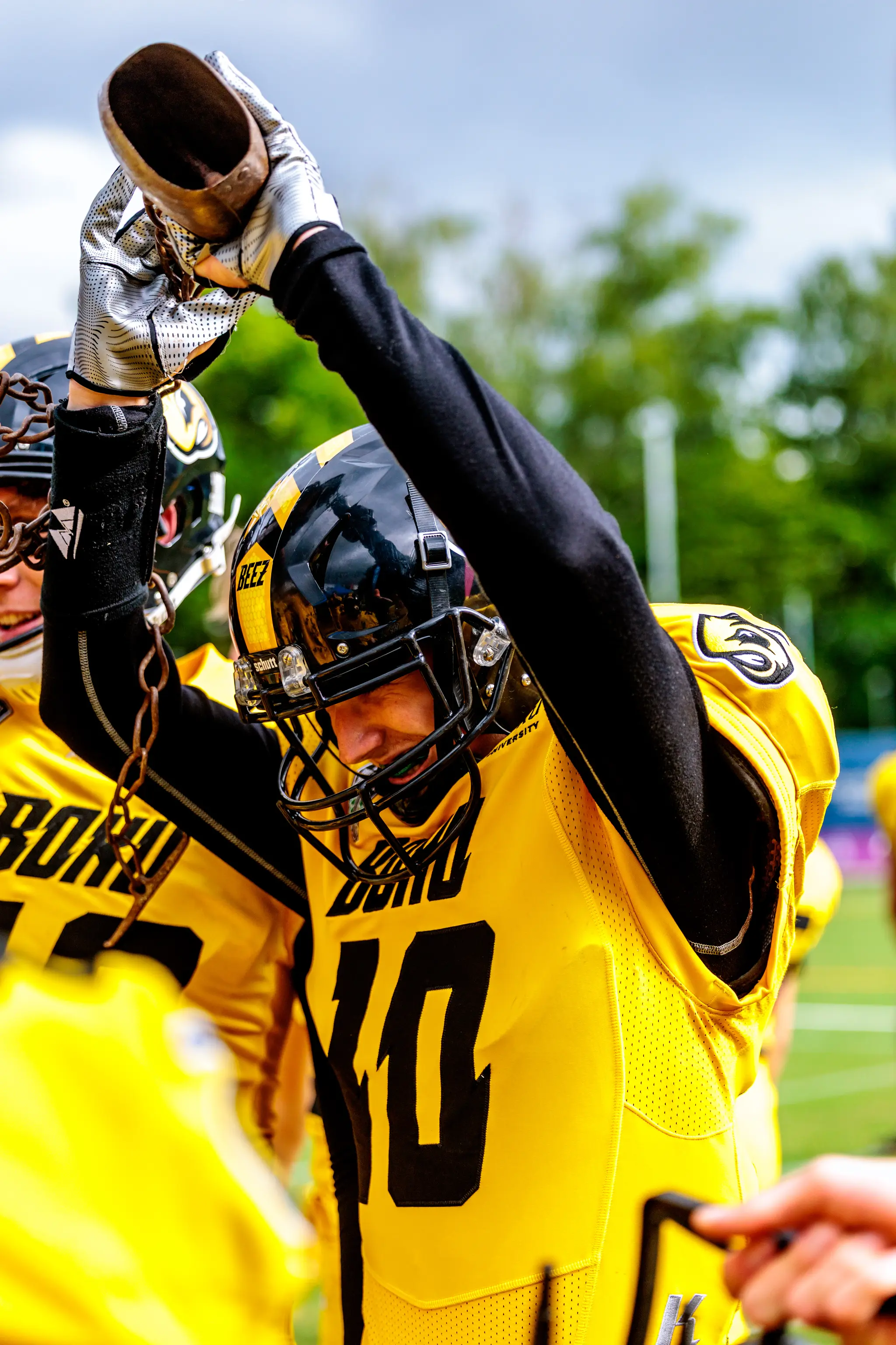 Ein American-Football-Spieler in gelb-schwarzer Uniform feiert mit einer großen Metallglocke über dem Kopf 