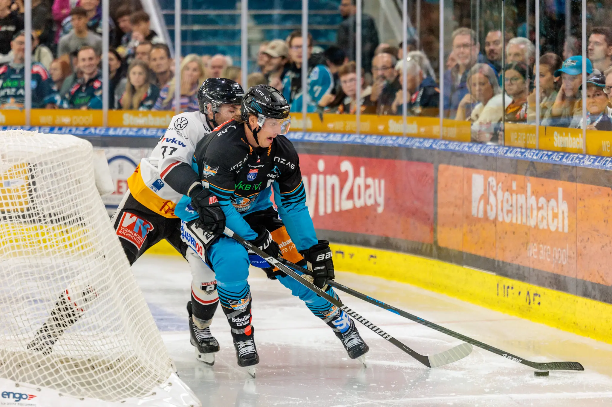 Eishockeyspieler Emilio Romig der Black Wings Linz kämpft mit einem Gegenspieler der Pioneers Vorarlberg vor dem Tor um den Puck