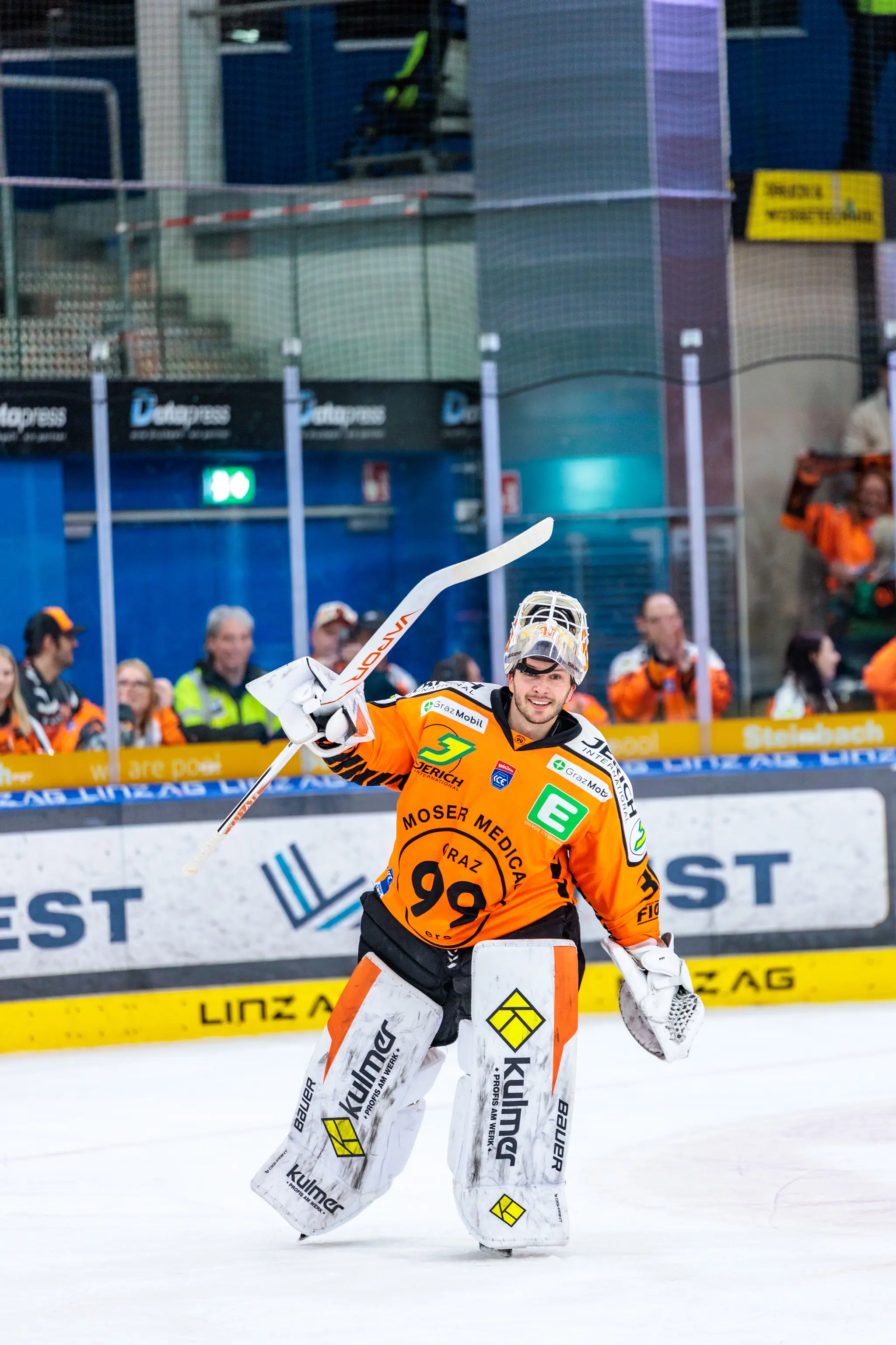 Ein Eishockey-Torwart der Grazer 99ers im orangefarbenen Trikot mit der Nummer 99 jubelt auf dem Eis und hält seinen Schläger in die Höhe