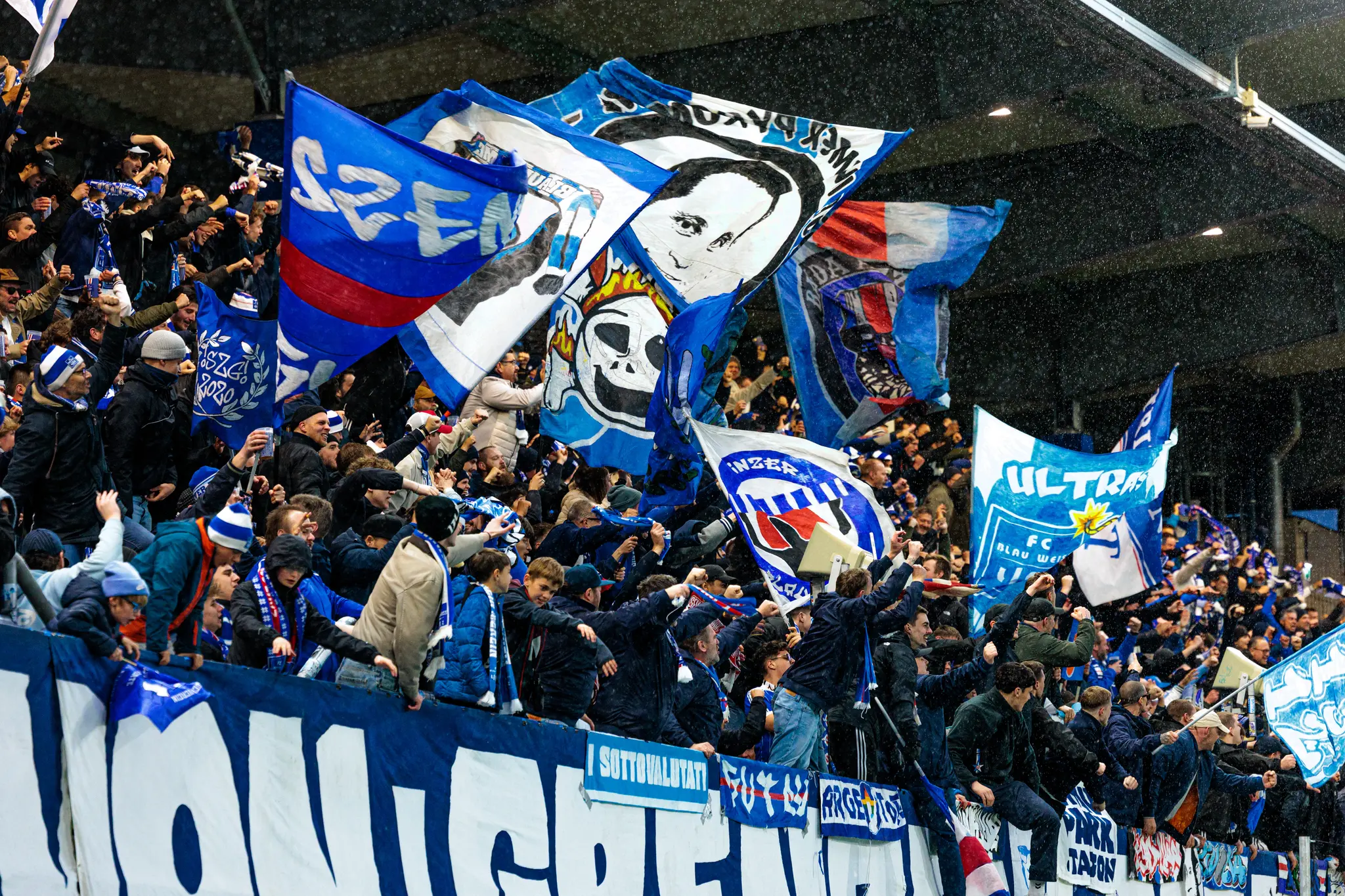 Jubelnde Fans des FC Blau-Weiß Linz schwenken große blau-weiße Fahnen und Banner im Stadion