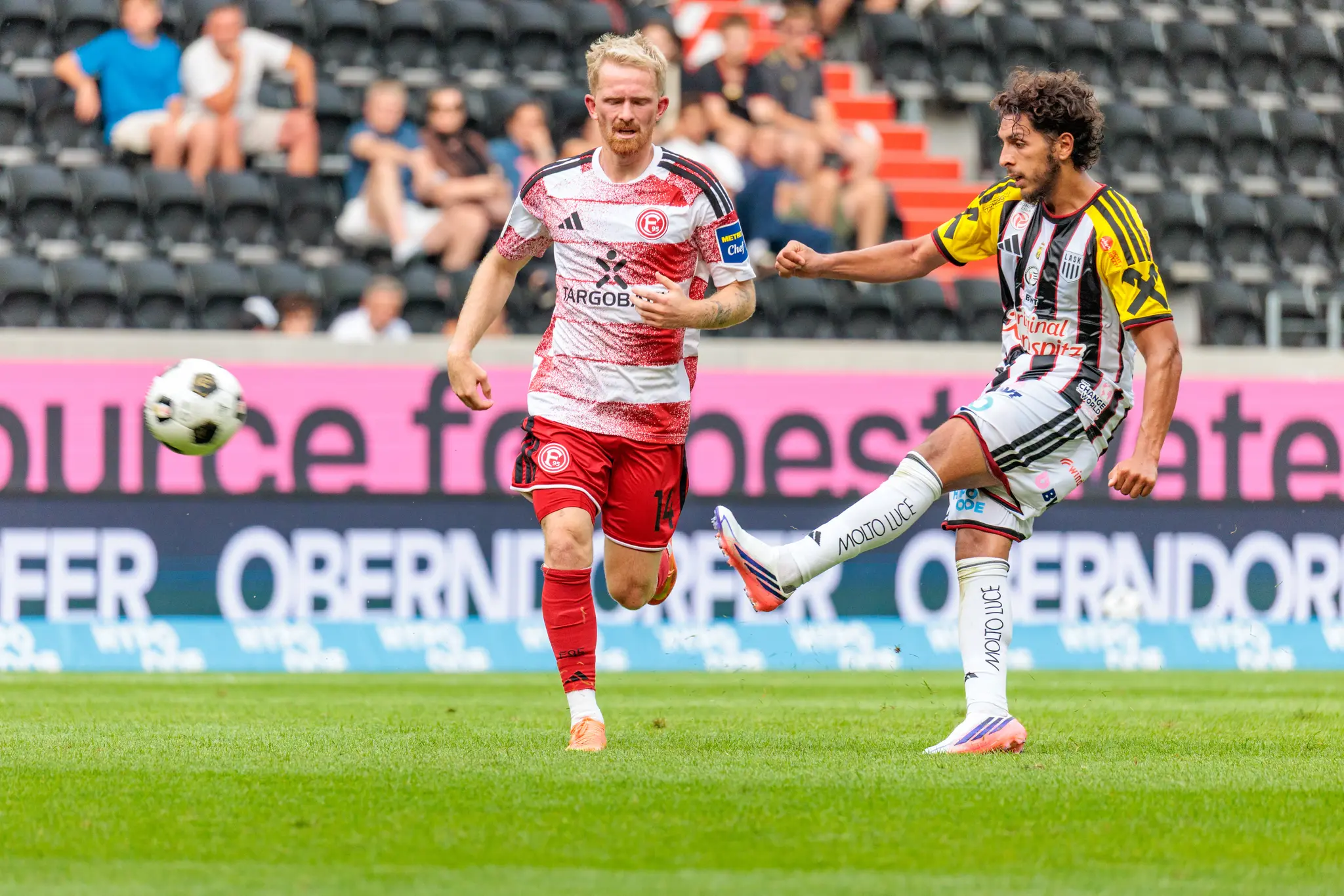 LASK-Spieler schlägt eine Flanke von der Seitenlinie in den Strafraum, ein Düsseldorfer Verteidiger versucht zu blocken.