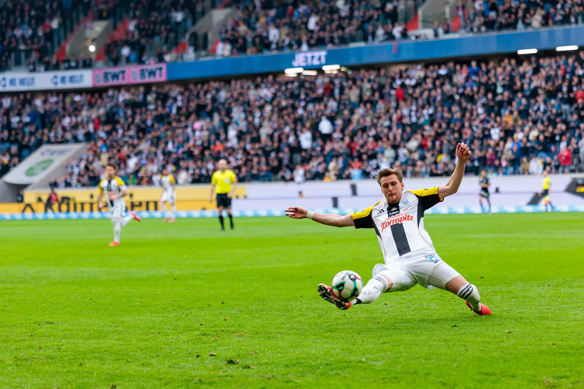 Ein LASK-Spieler streckt sich bei einem Versuch den Ball zu erreichen knapp über dem Gras