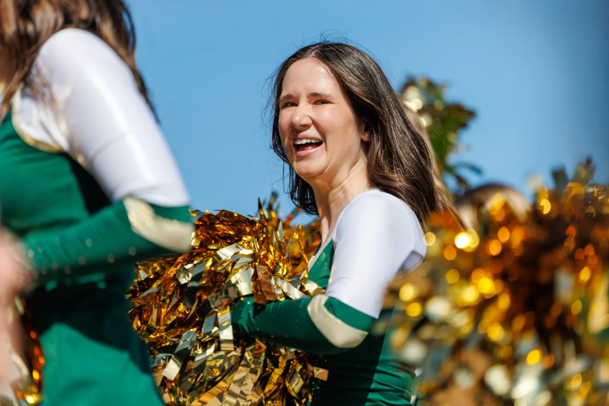Eine lächelnde Cheerleaderin der Premium Dancers hält glänzende goldene Pompoms bei einem Spiel der Danube Dragons in der Austrian Football League