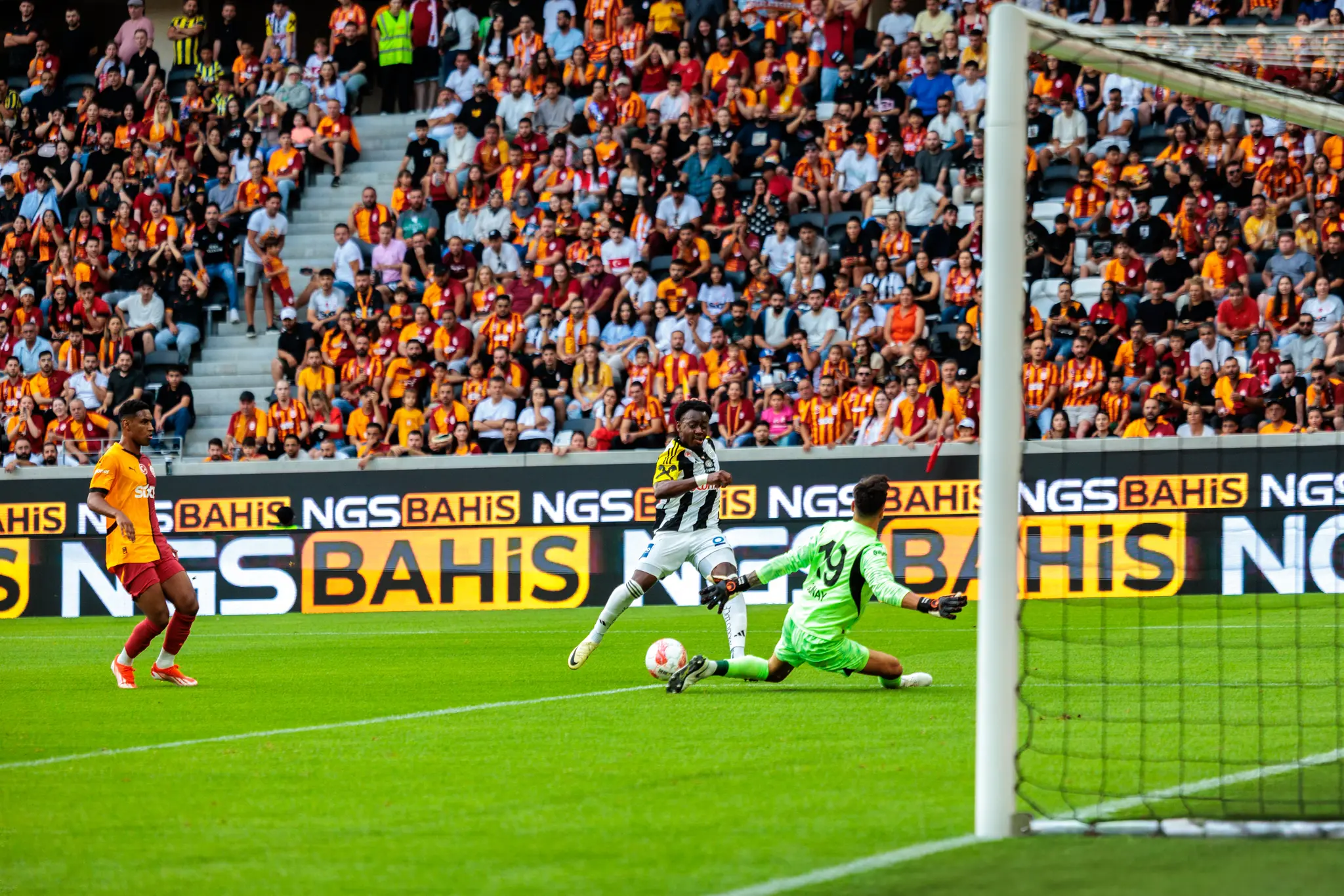 Ein dynamisches Fußballspiel zeigt einen Angreifer im schwarz-weißen Trikot des Lask Linz, der den Ball auf das Tor schießt, während der Torhüter von Galatasaray Istanbul im grünen Trikot abwehrt 