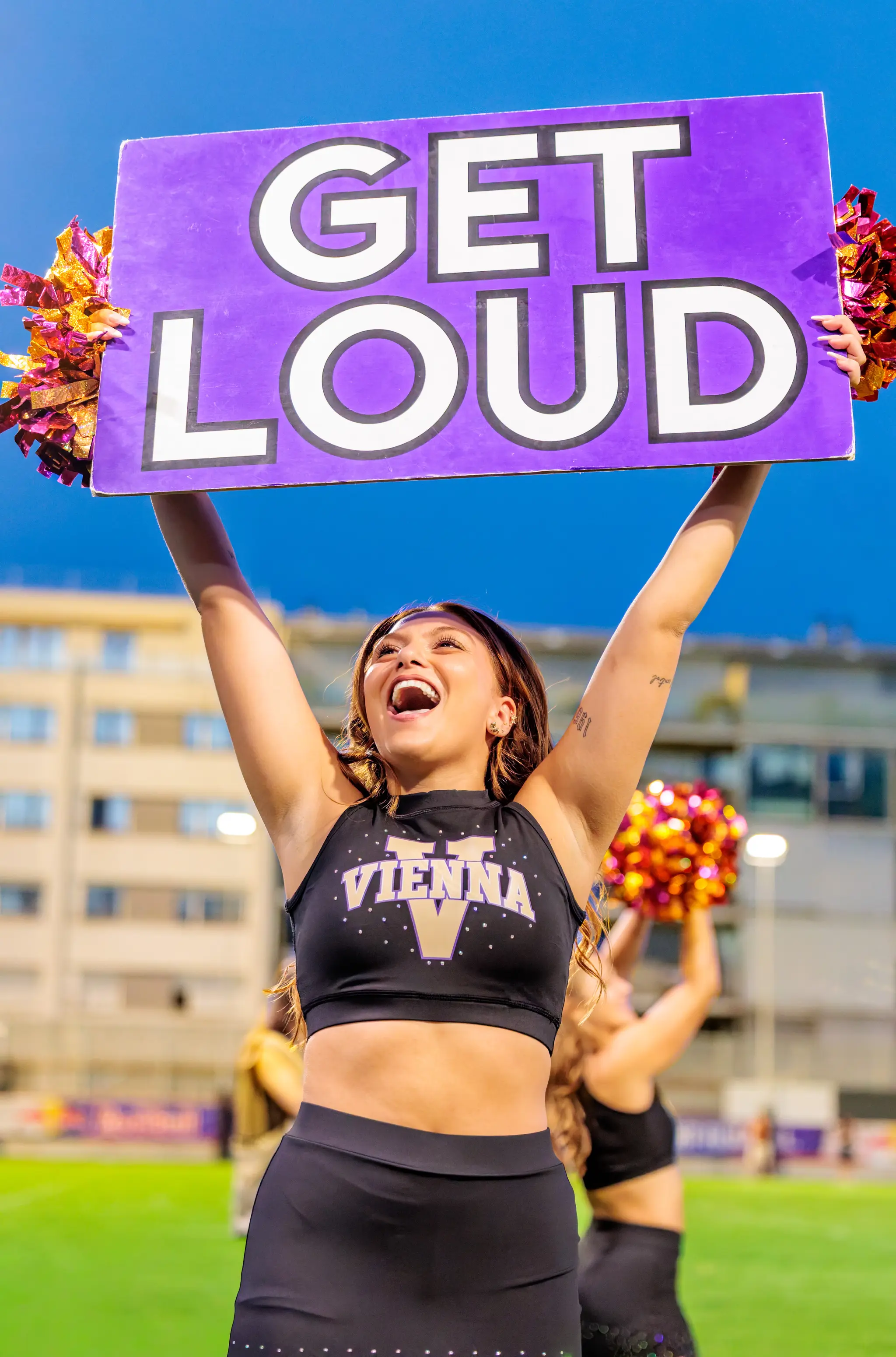 Mit beiden Händen hält eine Tänzerin des Vienna Vikings Cheer Squads das lila „GET LOUD“-Schild über den Kopf und heizt dem Publikum ein.