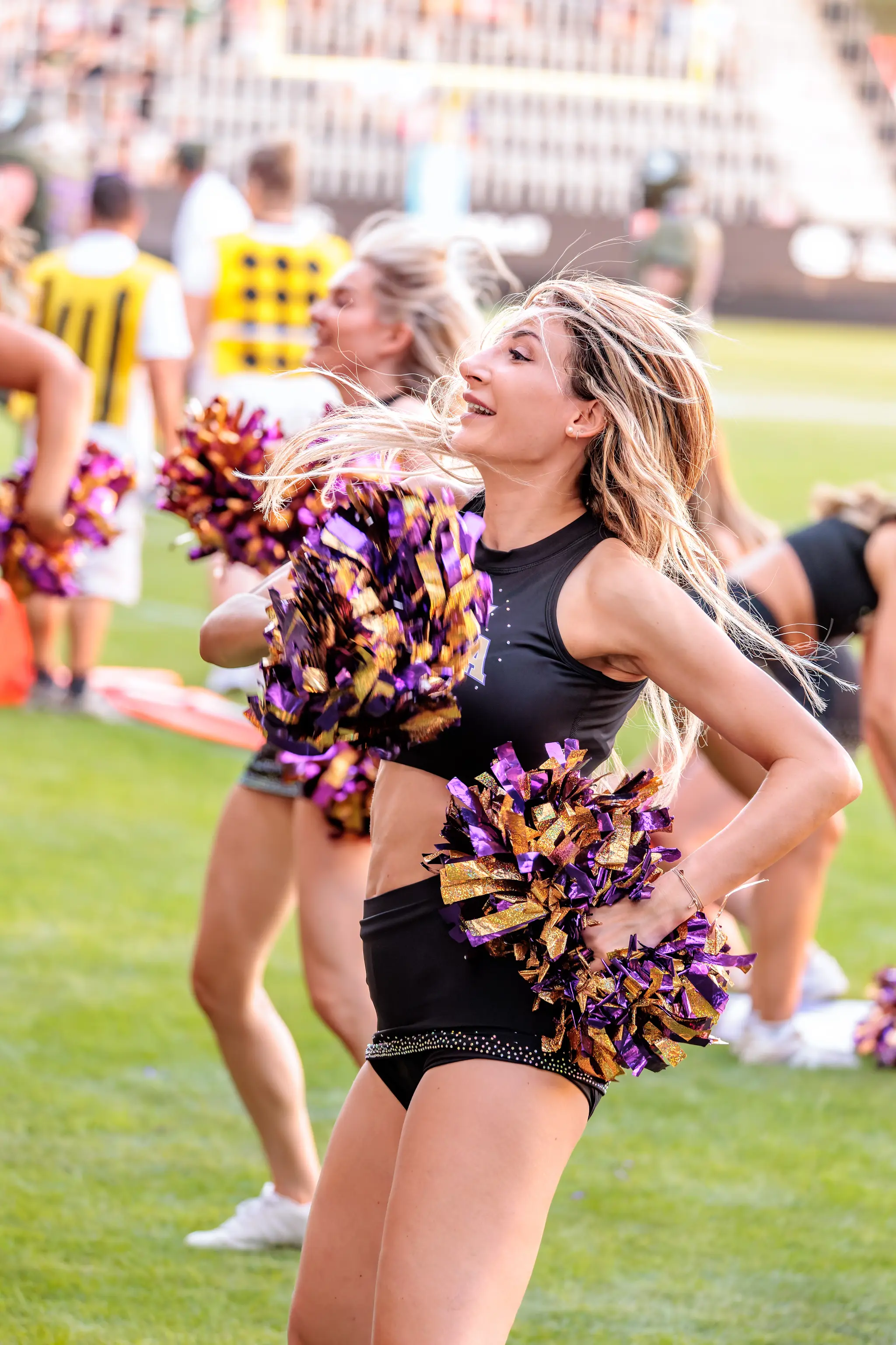 Cheerleaderin des Spirit Squad in schwarzem Outfit bei einer Tanzhaltung mit Pompons.
