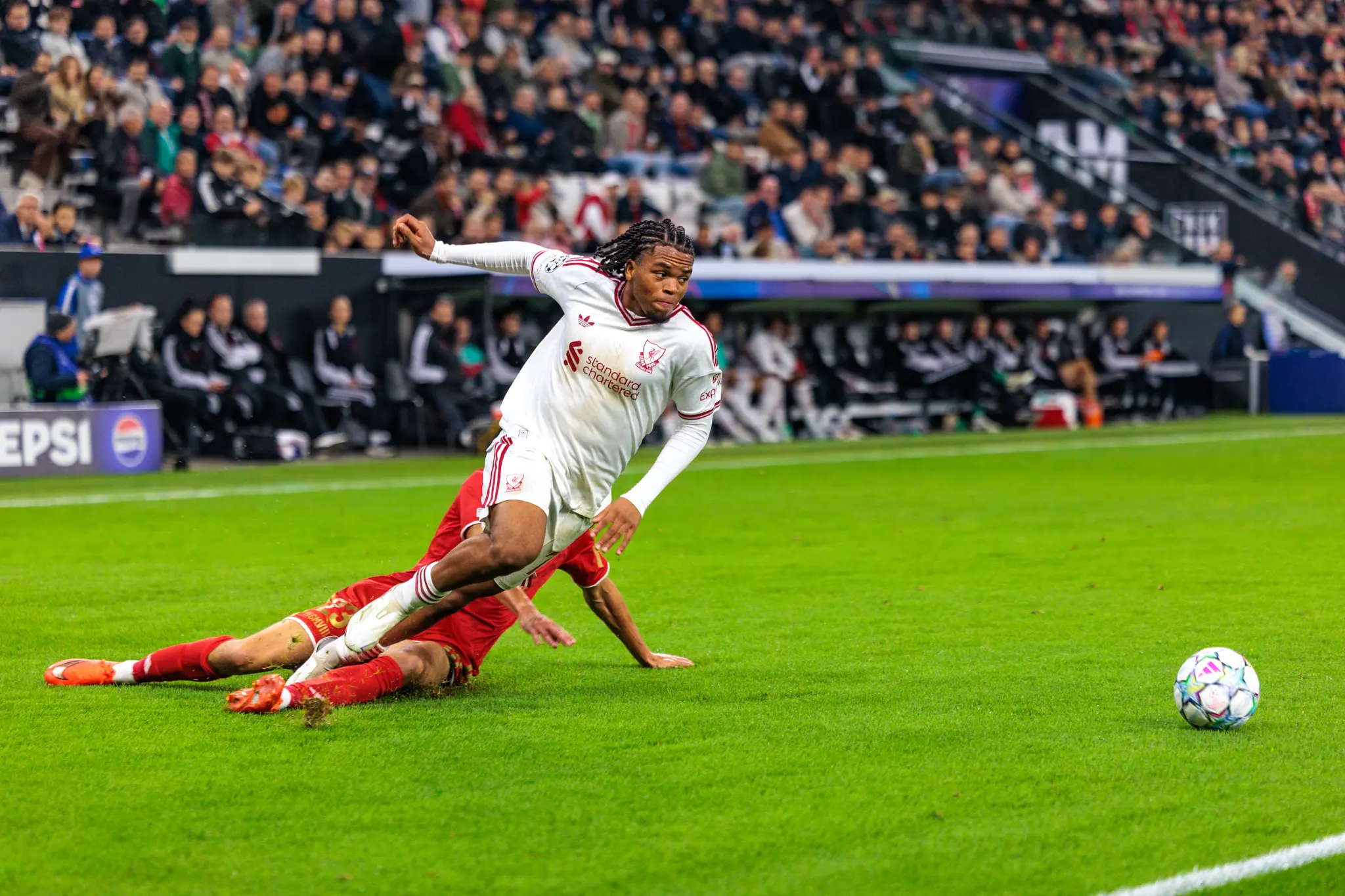 Ein Liverpooler Spieler läuft an dem auf dem Rasen nachrutschenden Daniel Elfadli (23) vorbei, dahinter sind Ersatzbank und Tribüne zu sehen.