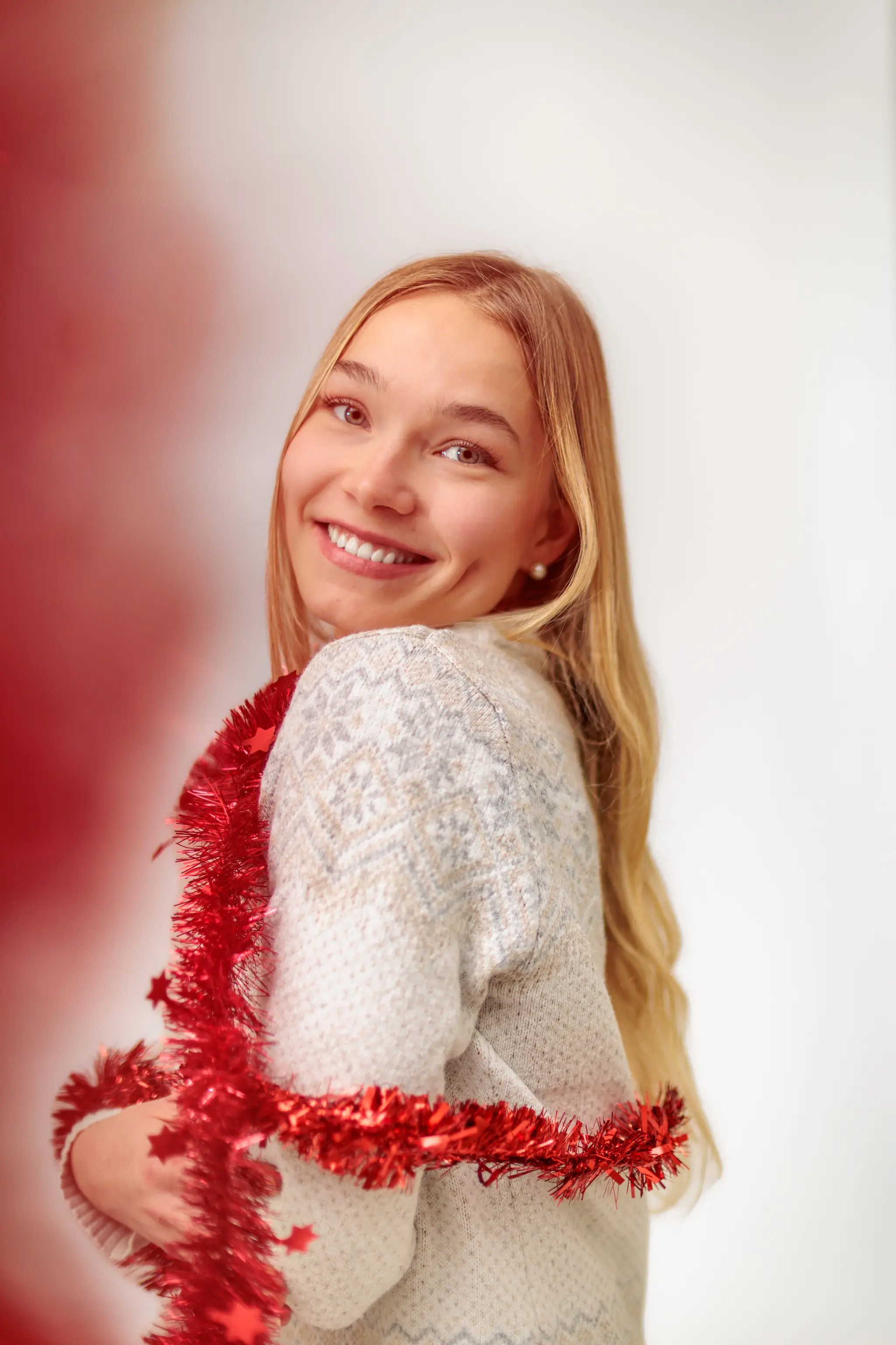 Das Model Kathrin blickt mit einem strahlenden Lächeln und einer roten Weihnachtsgirlande über der Schulter während eines festlichen Studio-Shootings in die Kamera