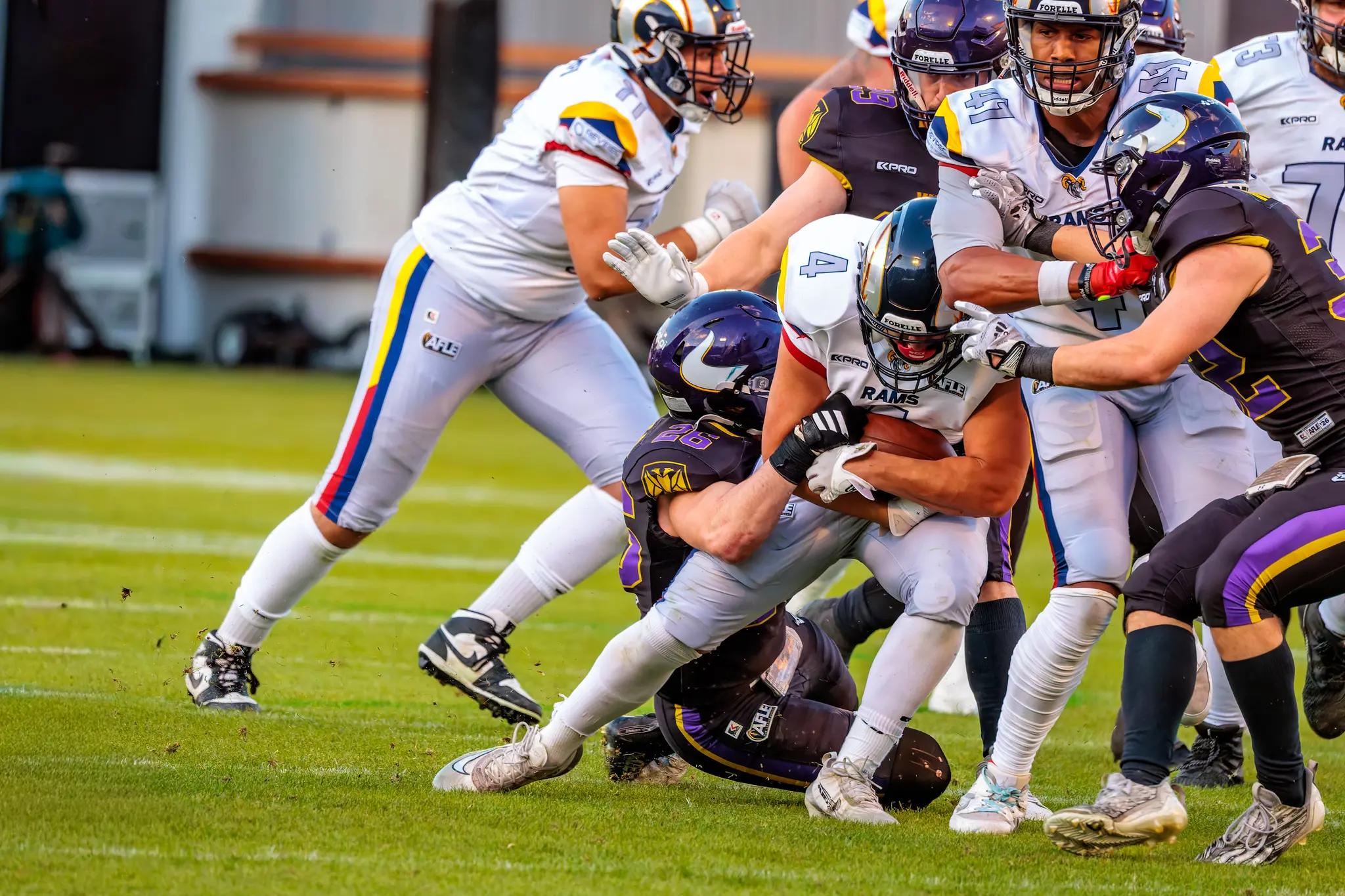 Ein Spieler der Vienna Vikings wird von Verteidigern der Alpine Rams während eines intensiven Tacklings im AFLE-Spitzenspiel zu Boden gebracht