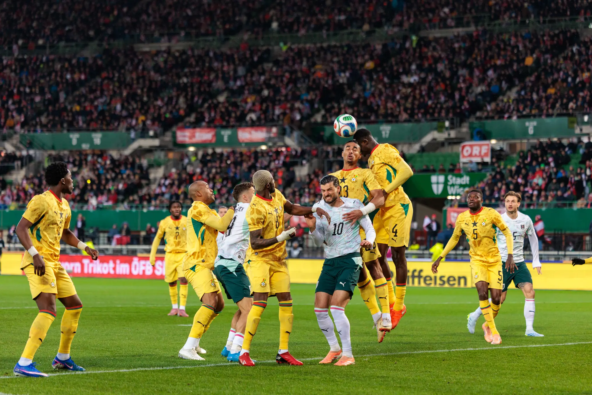 Fußballspieler aus Österreich und Ghana liefern sich ein intensives Kopfballduell um den Ball