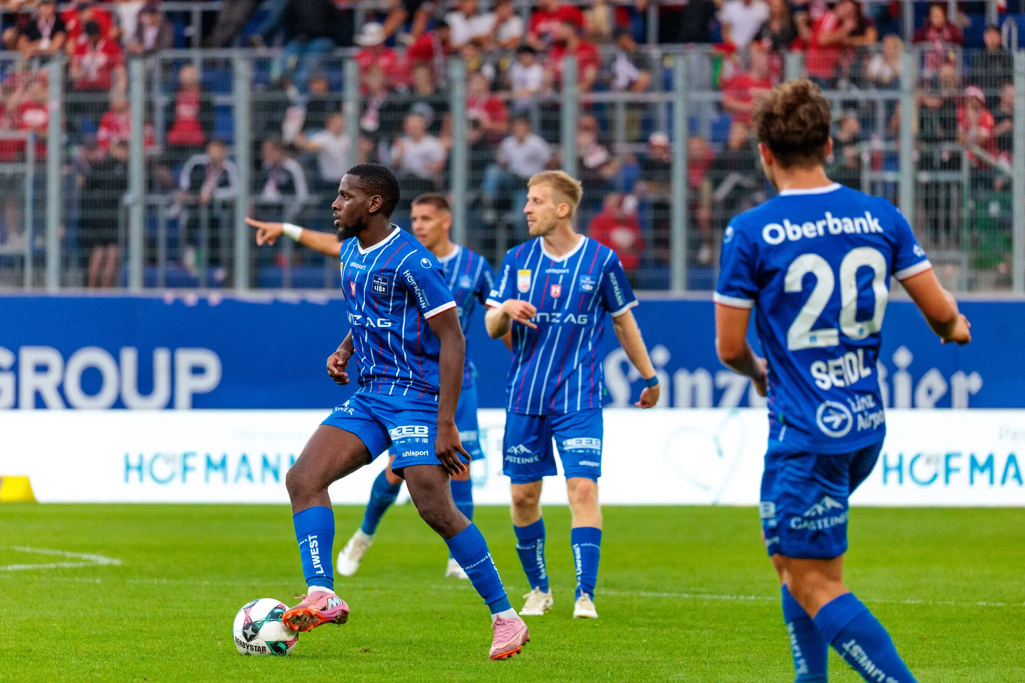 Mamadou Fofana vom FC Blau-Weiß Linz im blau-weiß-rot gestreiften Trikot kontrolliert mit seinen pinken Fußballschuhen den Ball während eines Spielaufbaus im Stadion